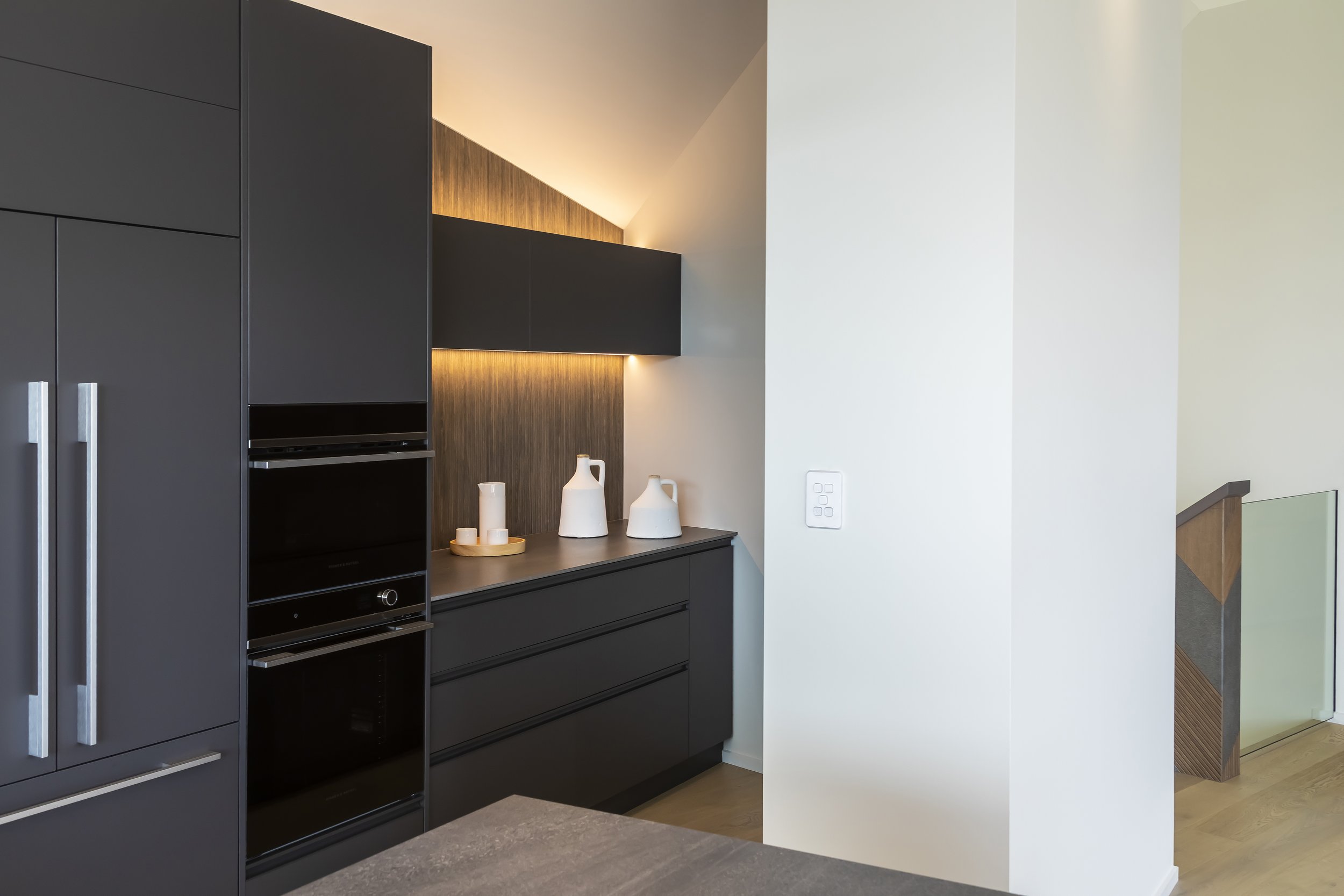 Modern kitchen corner with black cabinetry, decorative pottery, and subtle lighting. Kitchen Design by Bridget Coles Interior Design