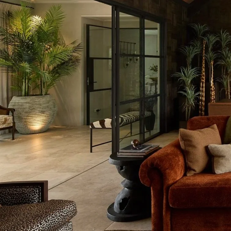 Interior living space with a large potted plant, glass doors, a bench, and an orange velvet sofa with pillows.
