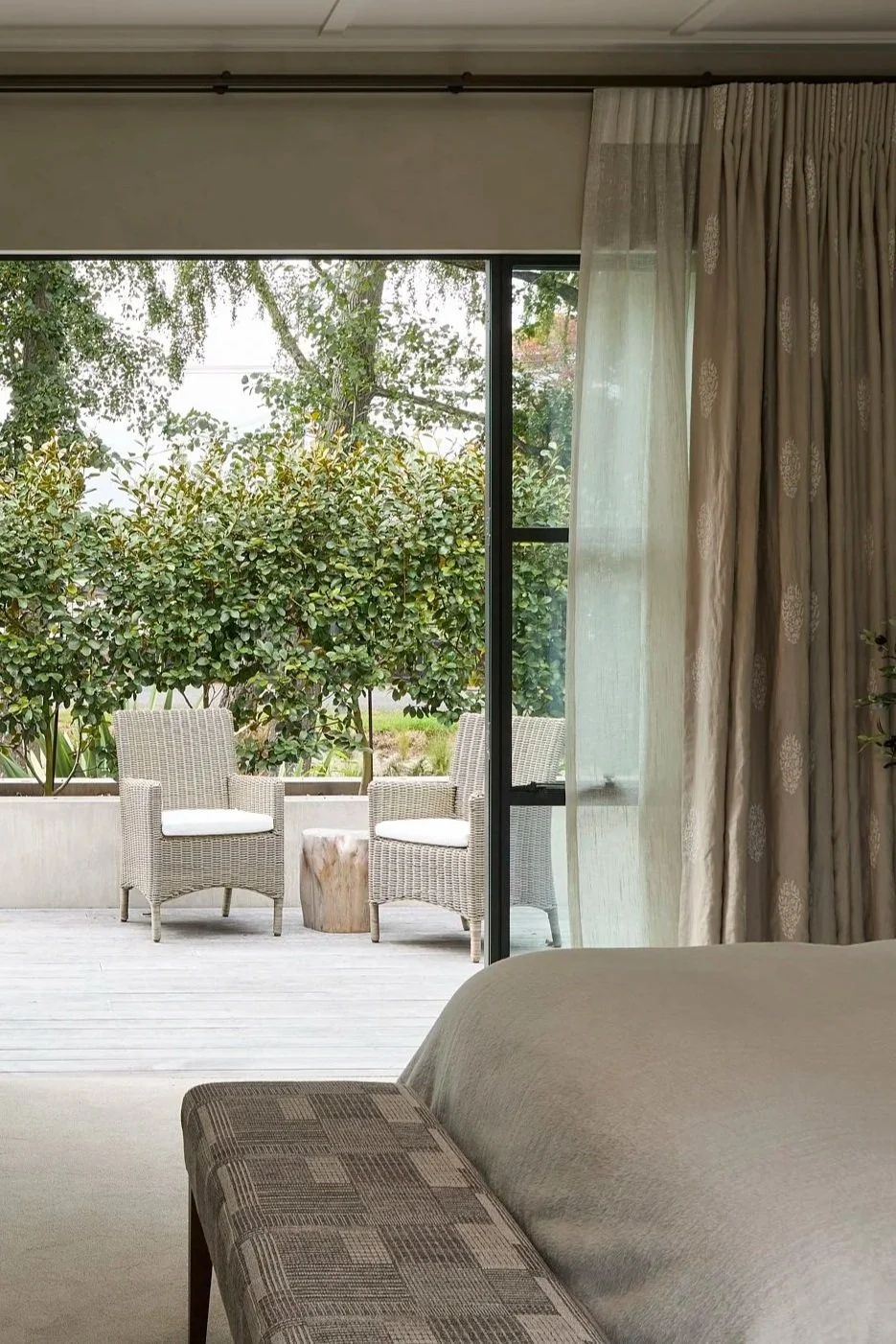 Living room with sliding glass door leading to an outdoor patio with wicker chairs, a small table, and green shrubbery. Romantic Sheer bedroom curtain.Linen paisly design curtain on a beautiful bronze rod