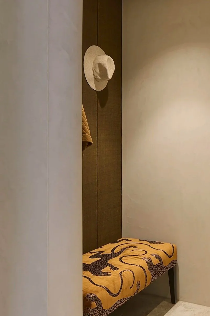 French Wallpaper coat area with a unique ottoman that has a panther on it in gold velvet A beige hat hanging on a hook on a dark wooden wall, with a tan quilted coat partially visible. 