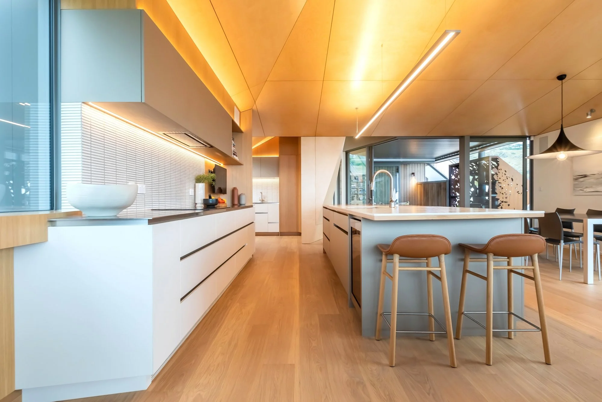 Modern open-concept kitchen and dining area with wooden floors, white cabinets, a large island, and large windows letting in natural light.