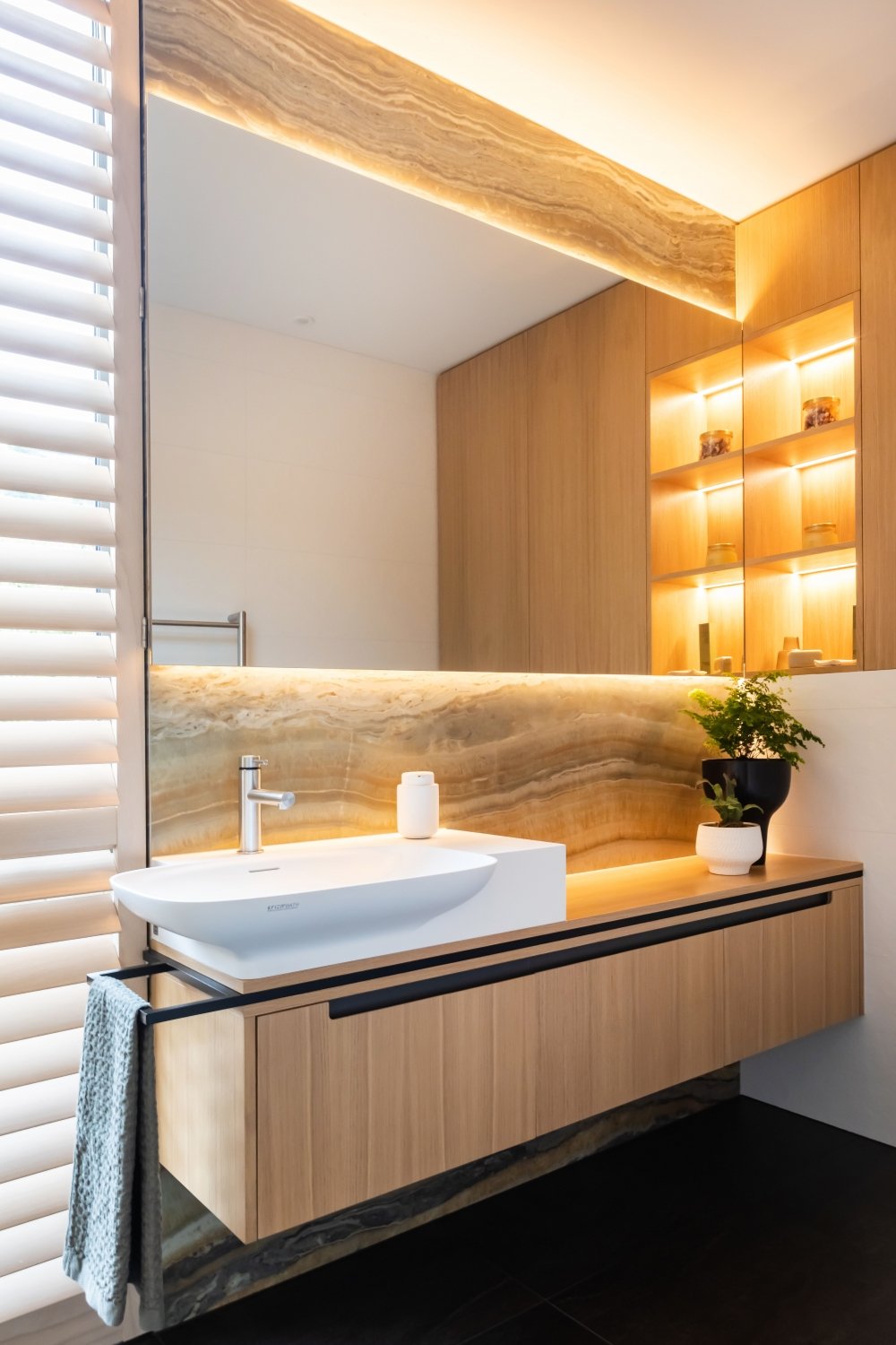 Modern bathroom with a wooden vanity, white sink, large mirror, potted plant, and built-in shelves with warm lighting Interior design Bridget Coles Interior Design Christchurch BCSTUDIO