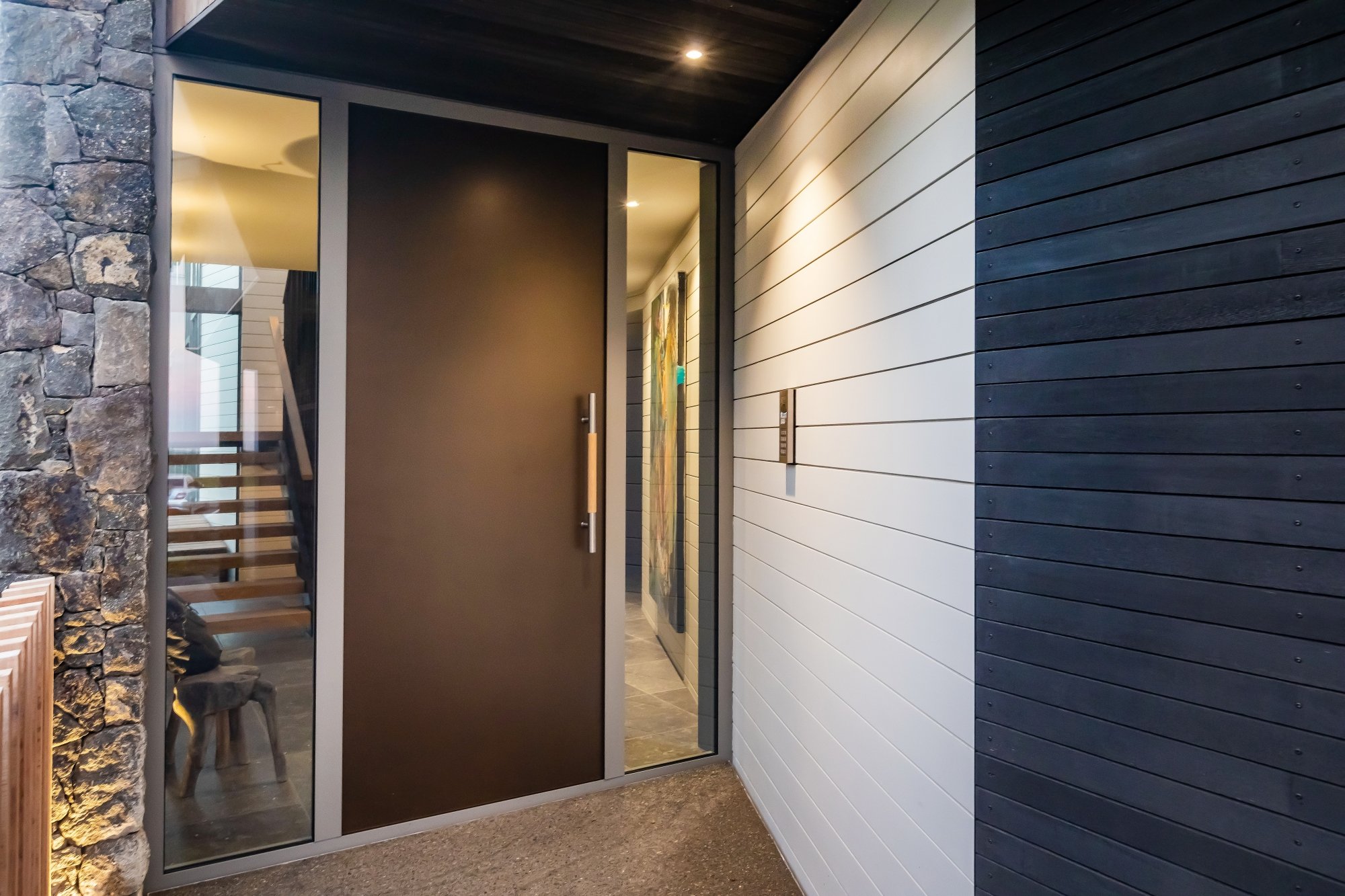 Modern entrance hallway with a Dulux powdercoated door, glass panels, and mixed wall textures of stone, white, and black wood siding.