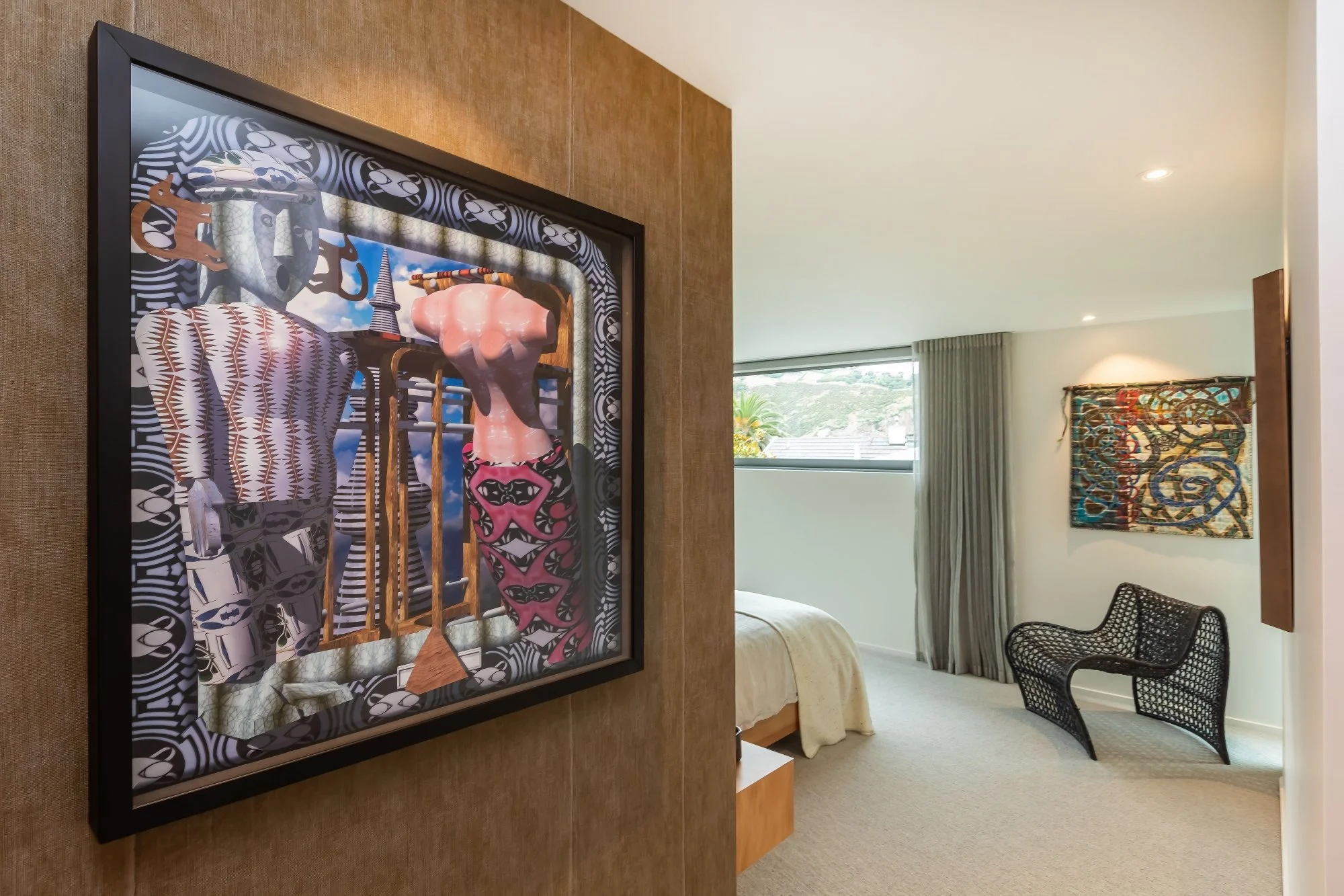 Framed colorful artwork hanging on a beige wall in a modern living space with a bed, curtains, and a black chair.