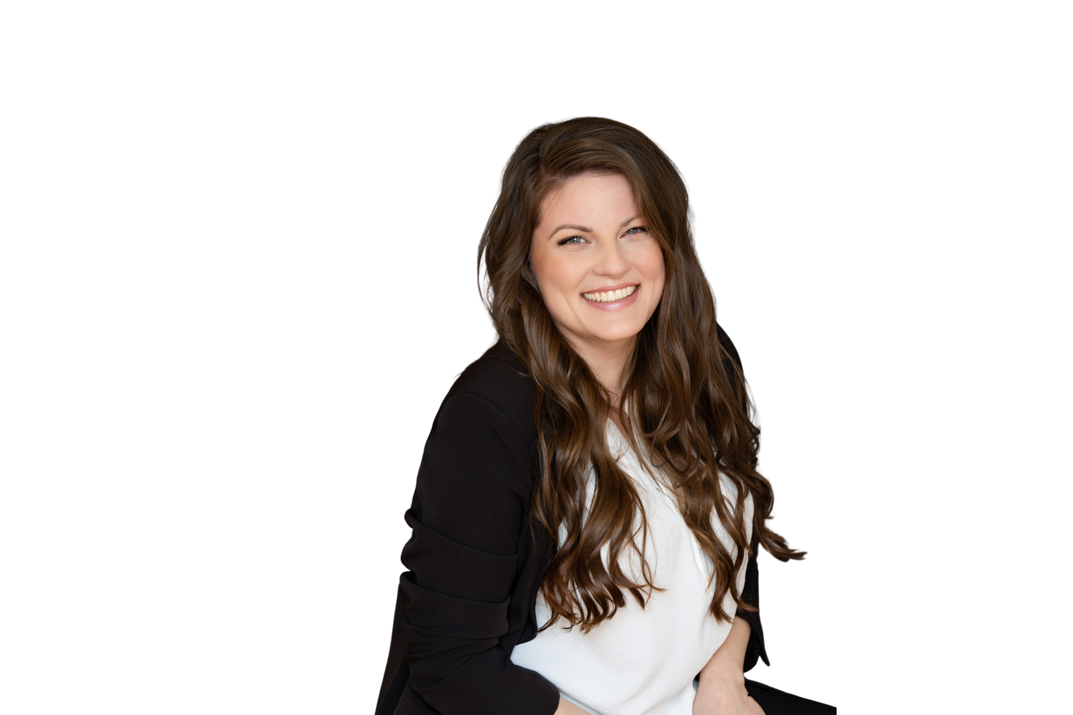 Smiling woman with long, wavy brown hair, wearing a white top and black blazer, sitting against a plain background.