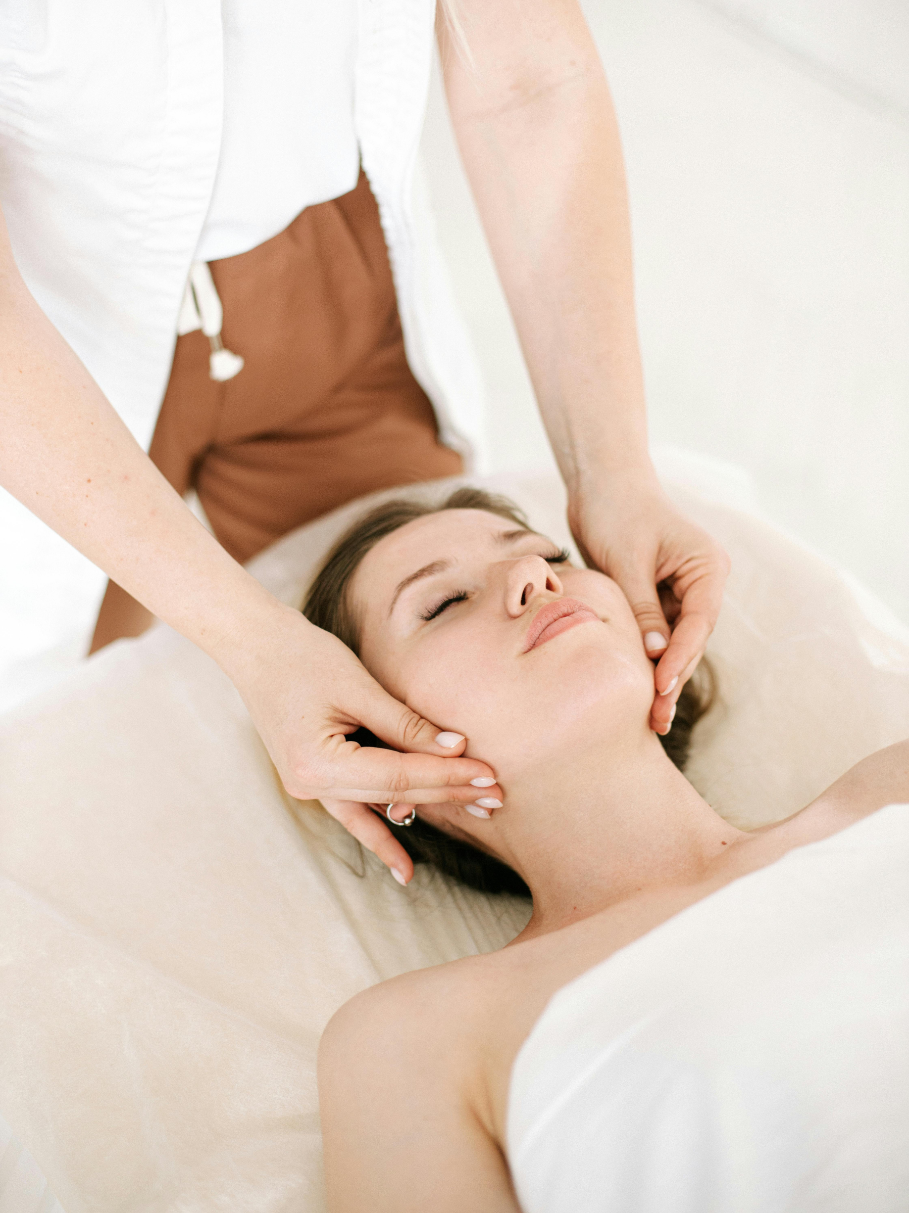 A woman receiving a facial massage from a massage therapist in a spa or massage therapy setting.