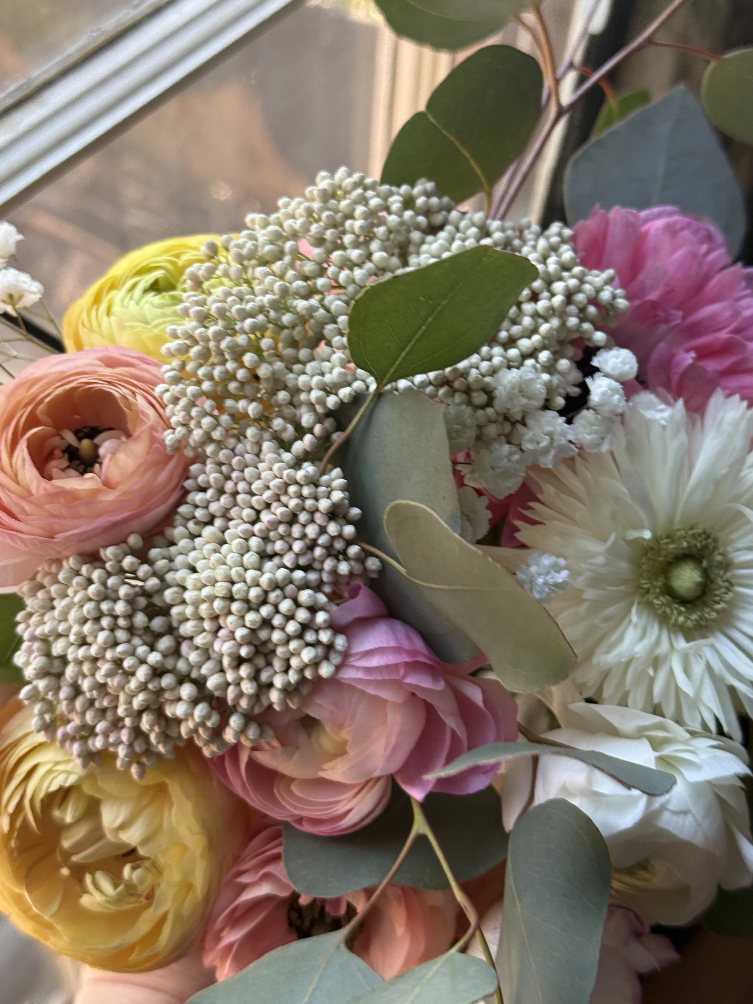 Close-up of a colorful bouquet of flowers with pink, yellow, white, and peach blooms, along with green leaves and eucalyptus.