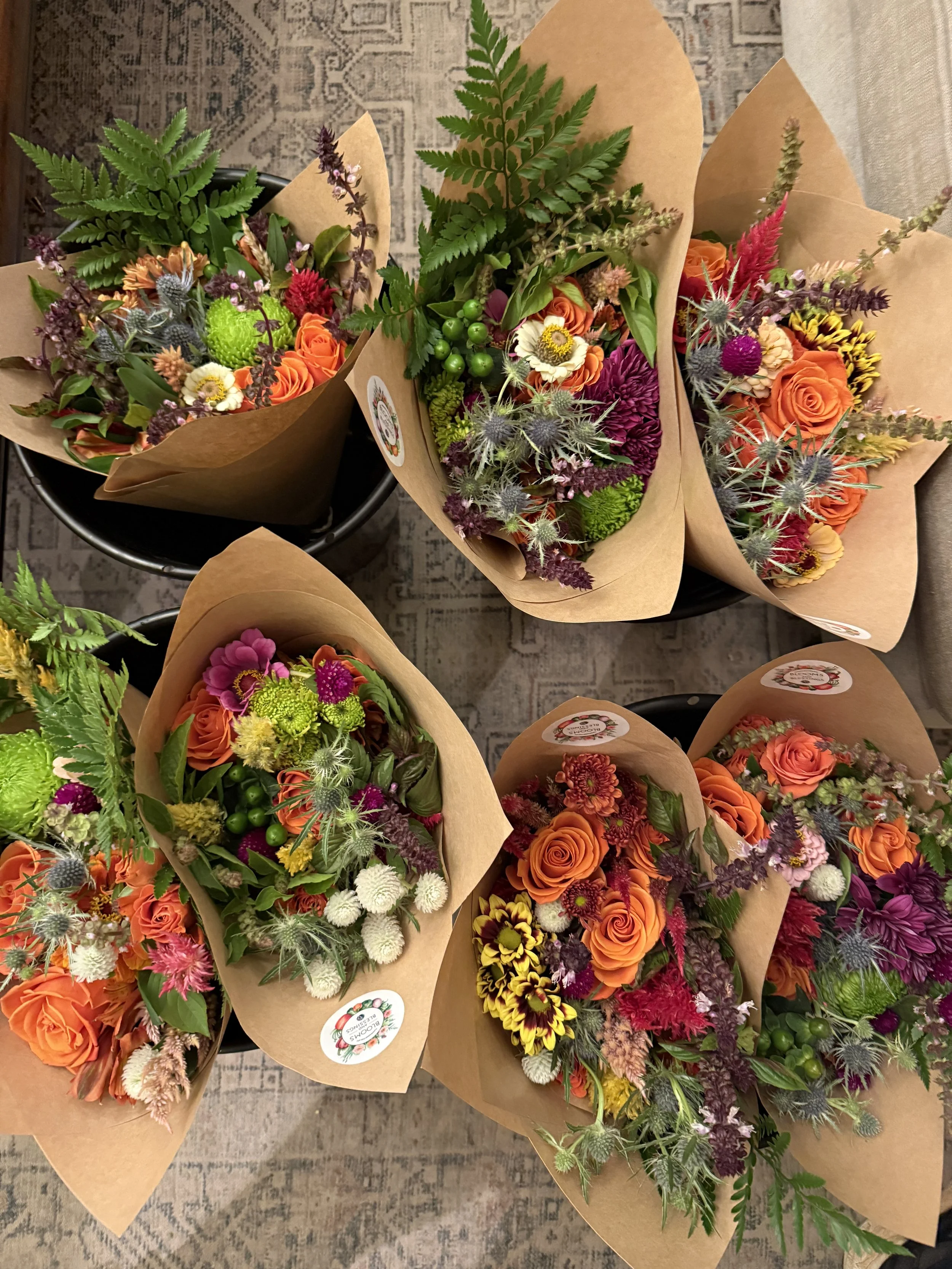 Multiple bouquets of colorful flowers wrapped in brown paper, placed on a patterned rug.