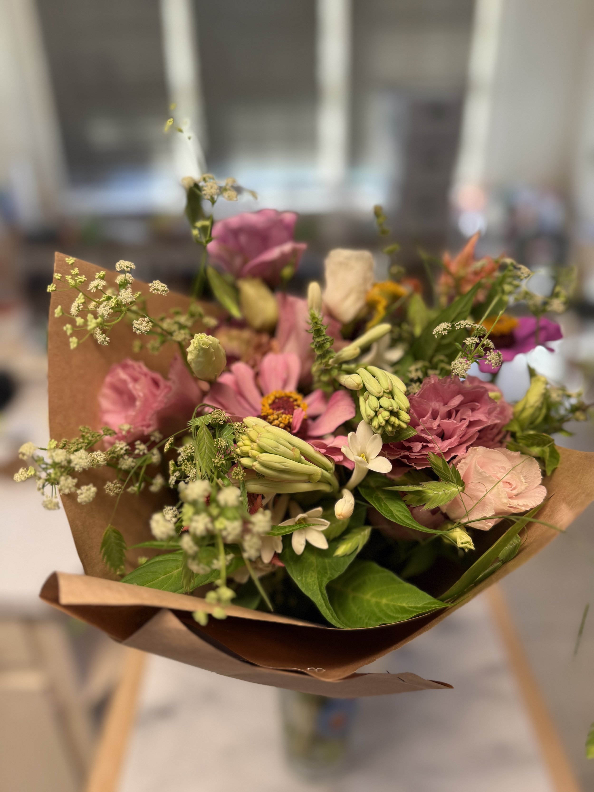 Colorful bouquet of pink, white, and yellow flowers wrapped in brown paper.