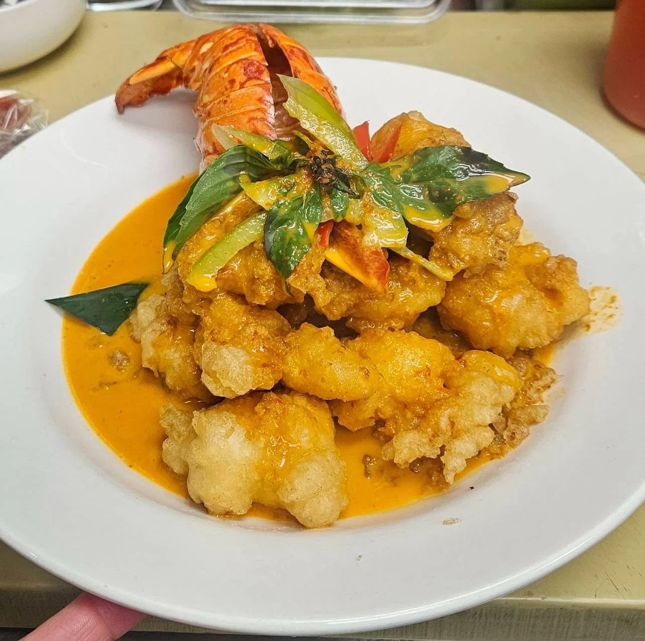 Fried seafood dish with a spicy orange sauce, garnished with basil, and a lobster tail on a white plate.