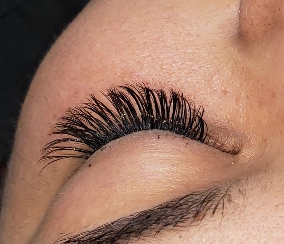 Close-up of a person's eye with eyelash extensions, showing the lashes in focus and the eyelid closed.