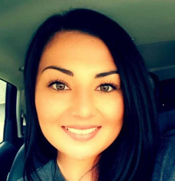 Close-up of a woman with dark hair, smiling, inside a vehicle.