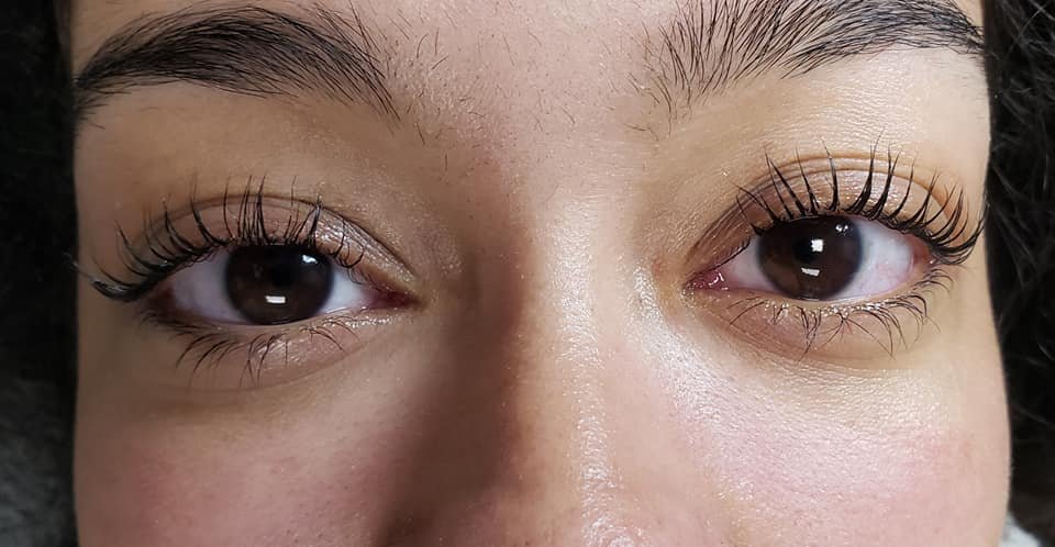 Close-up of a person's eyes with eyelashes extensions, slightly open, showing brown irises.