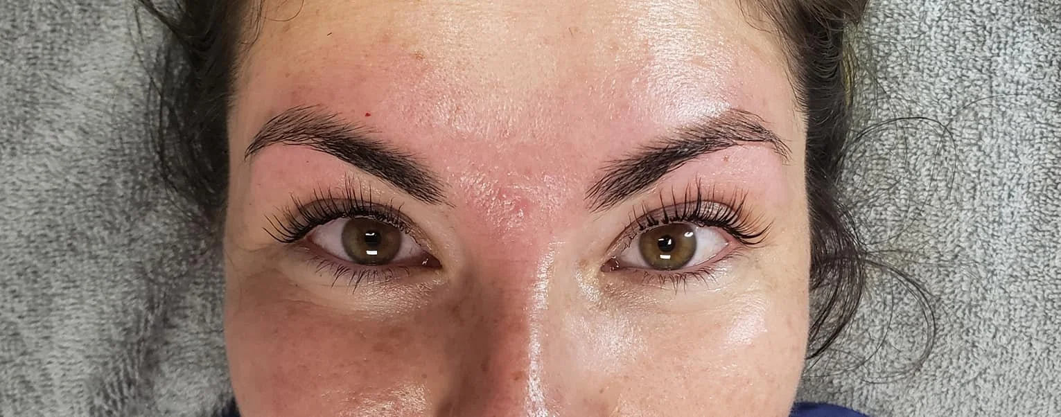Close-up photo of a woman's face with eyelash extension focusing on her beautified eyes and eyebrows, with makeup and hair pulled back.