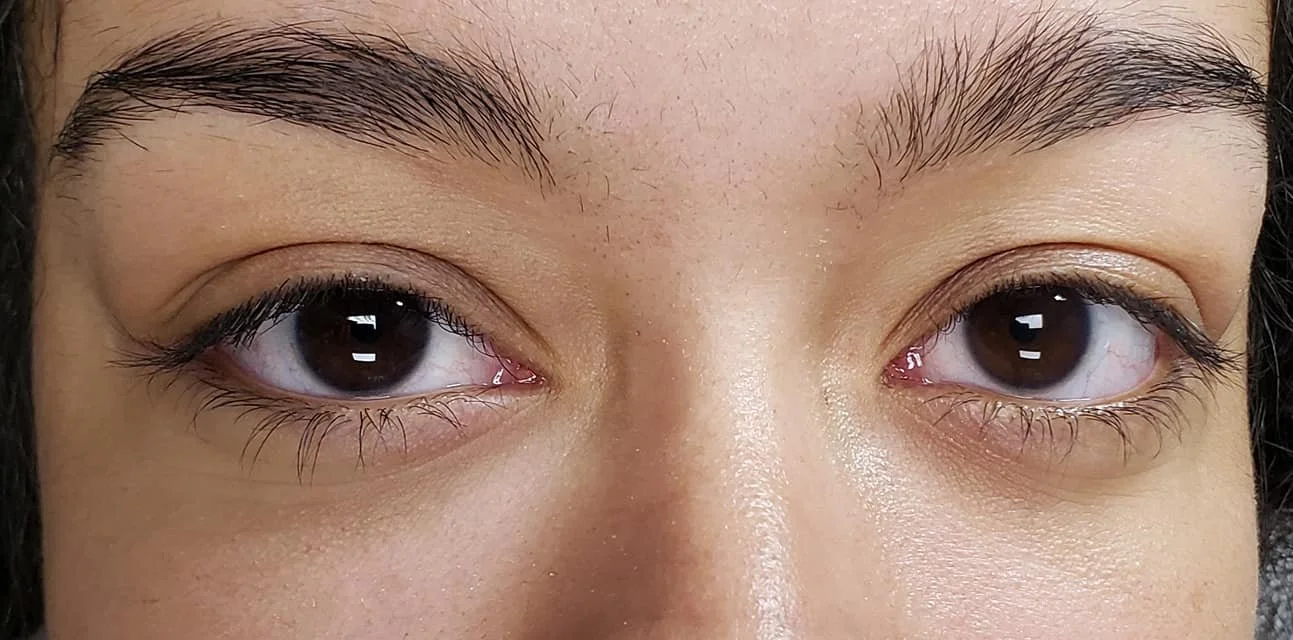Close-up of a person's face before eyelash extension showing their eyes, eyebrows, and part of the nose, with a natural skin tone and dark hair.