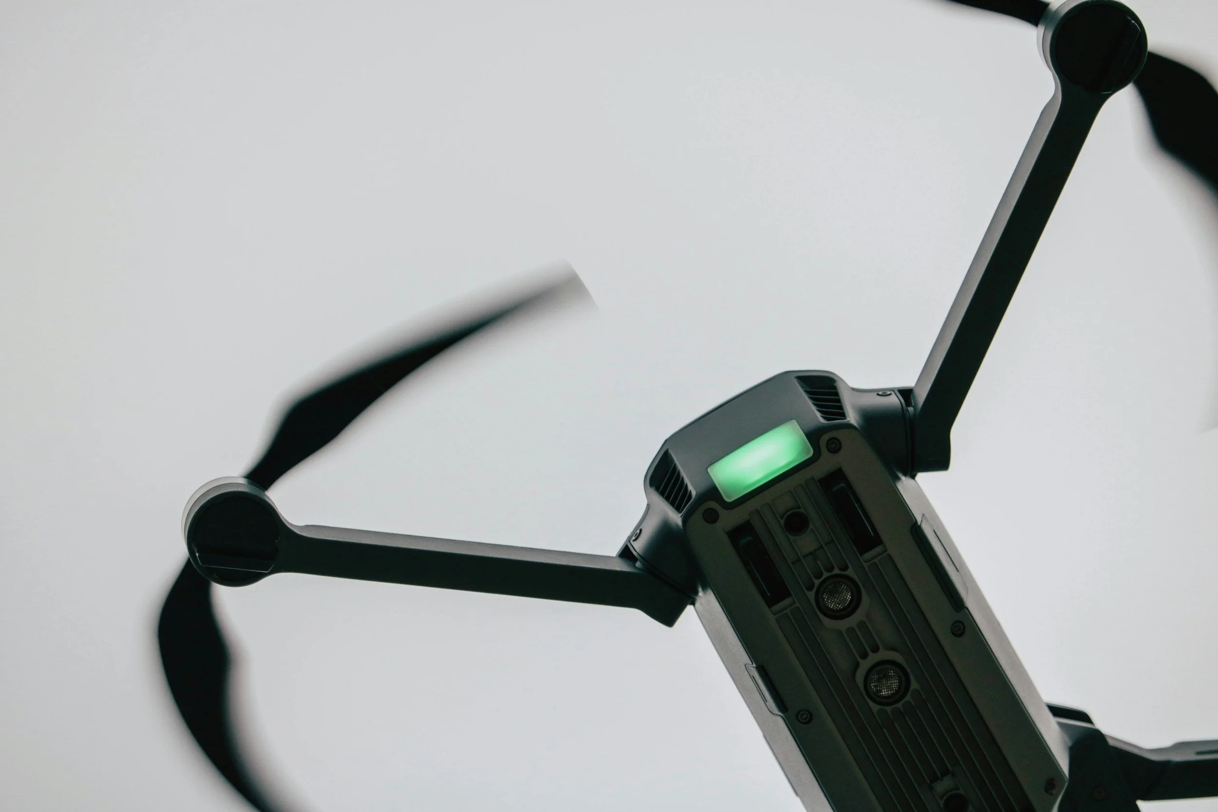 Close-up of a drone with a green-lit display on the body and propellers in motion against a plain background.
