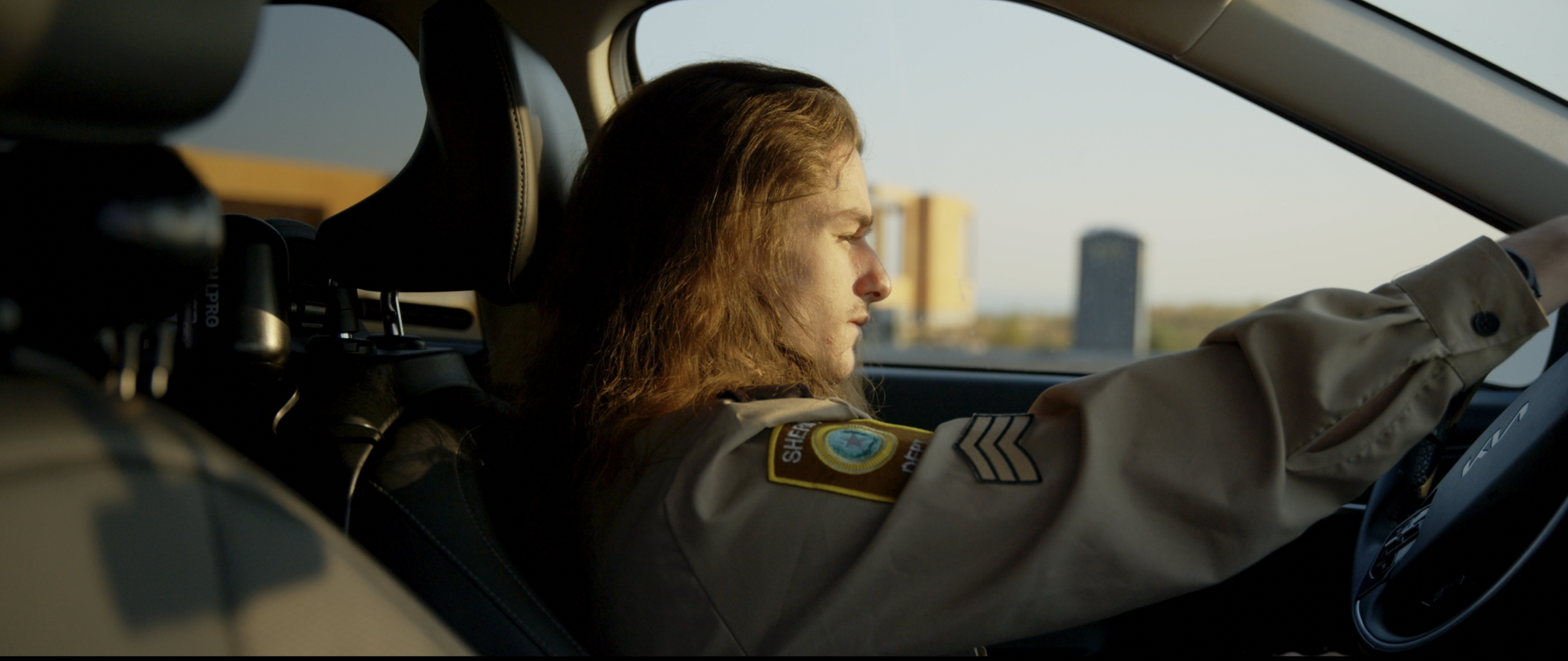 Lanson Duncan in a sheriff's uniform driving a car during sunset for ARC Lens Productions narrative film directed by Gurdil Dardi