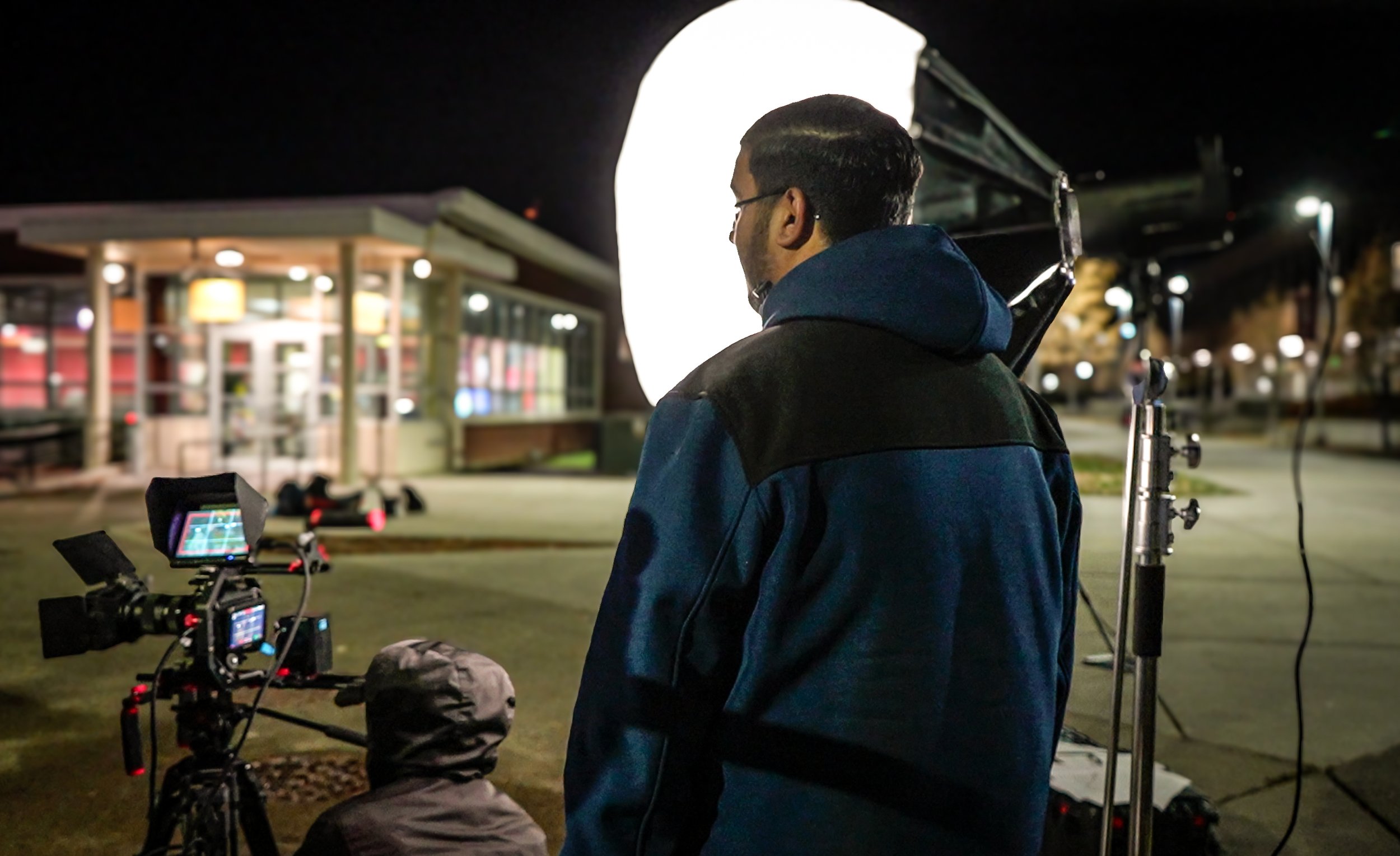 Film production crew preparing professional lighting and camera equipment for nighttime shoot as Gurdil Dardi watches as director.