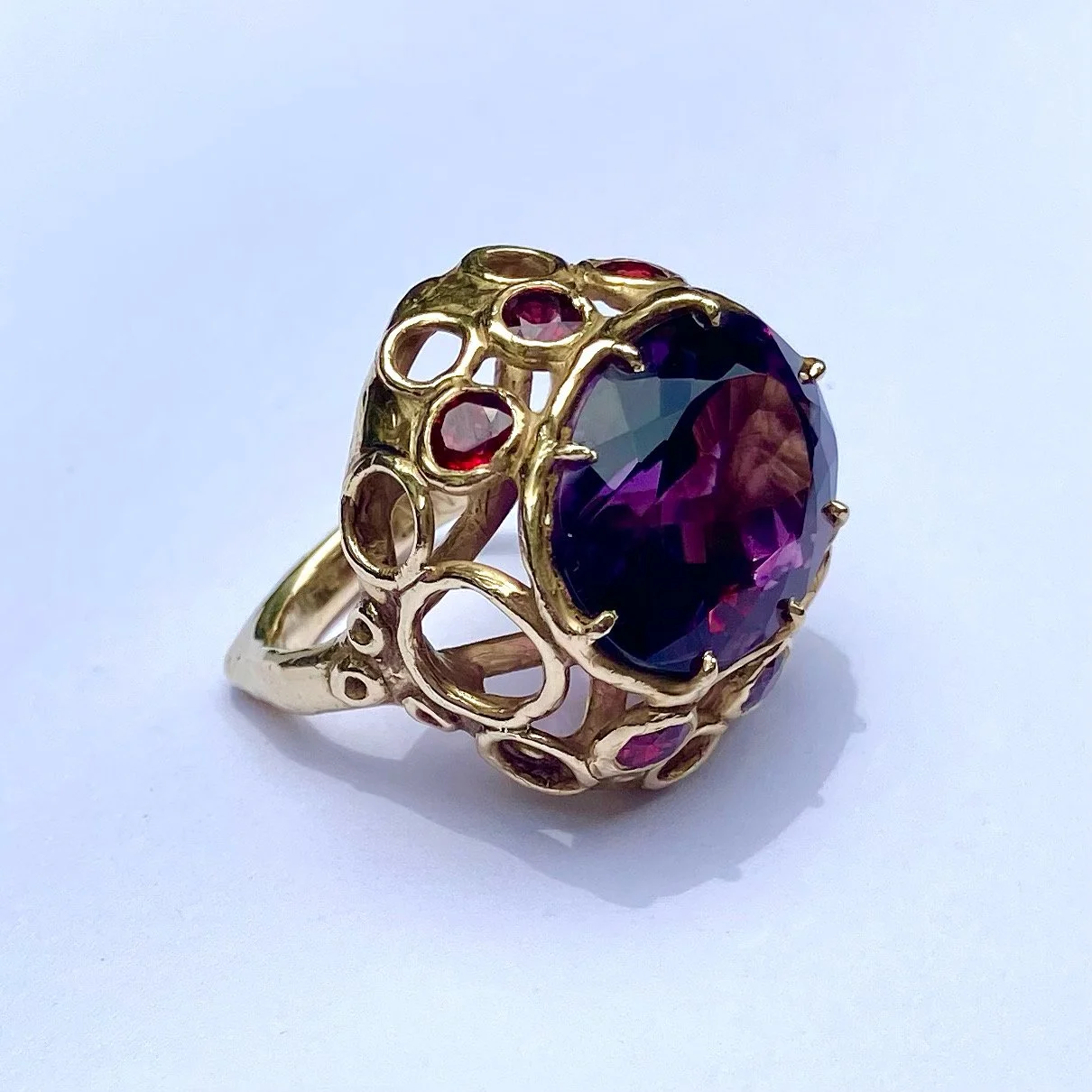 Gold ring with a large purple gemstone surrounded by smaller red stones, intricate openwork design
