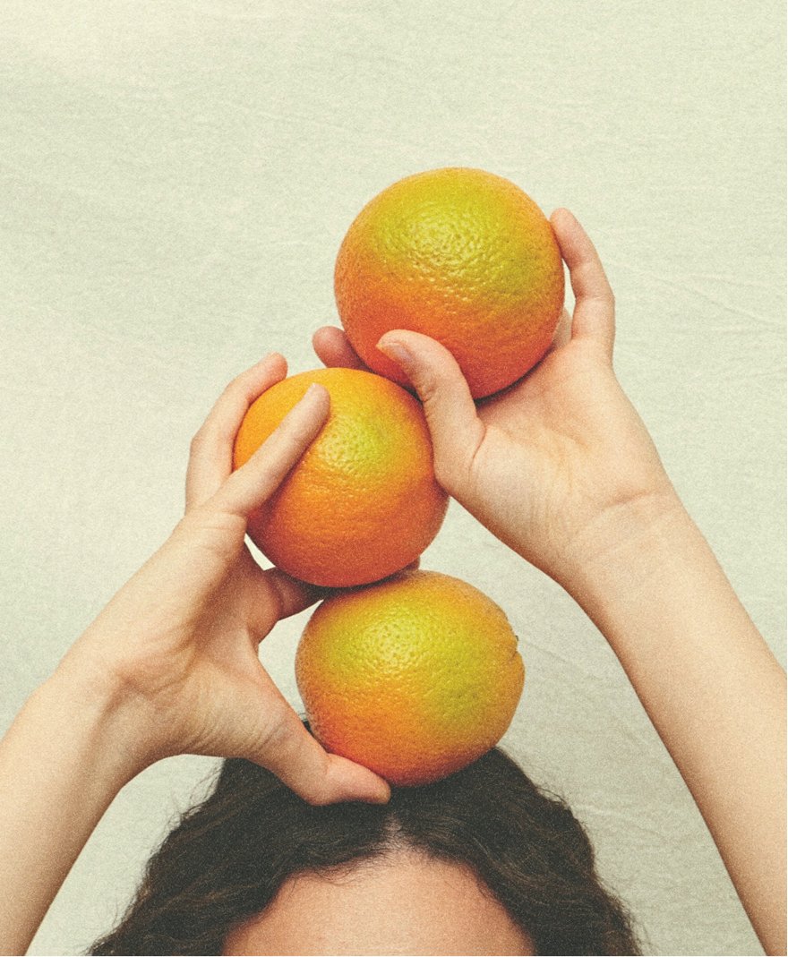Person stacking three oranges on their head against a plain background.