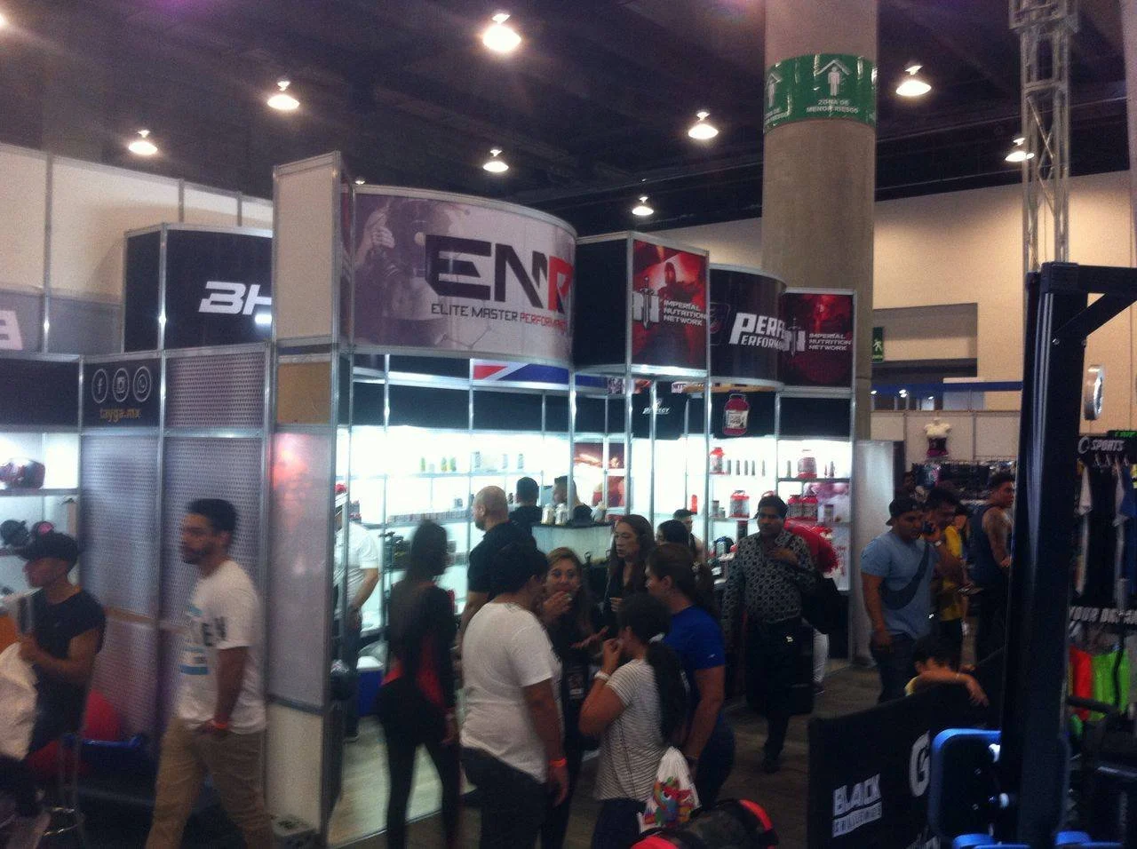 Personas en una feria o expo, con stands que exhiben productos relacionados con rendimiento y tecnología, algunos conversando y otros explorando.