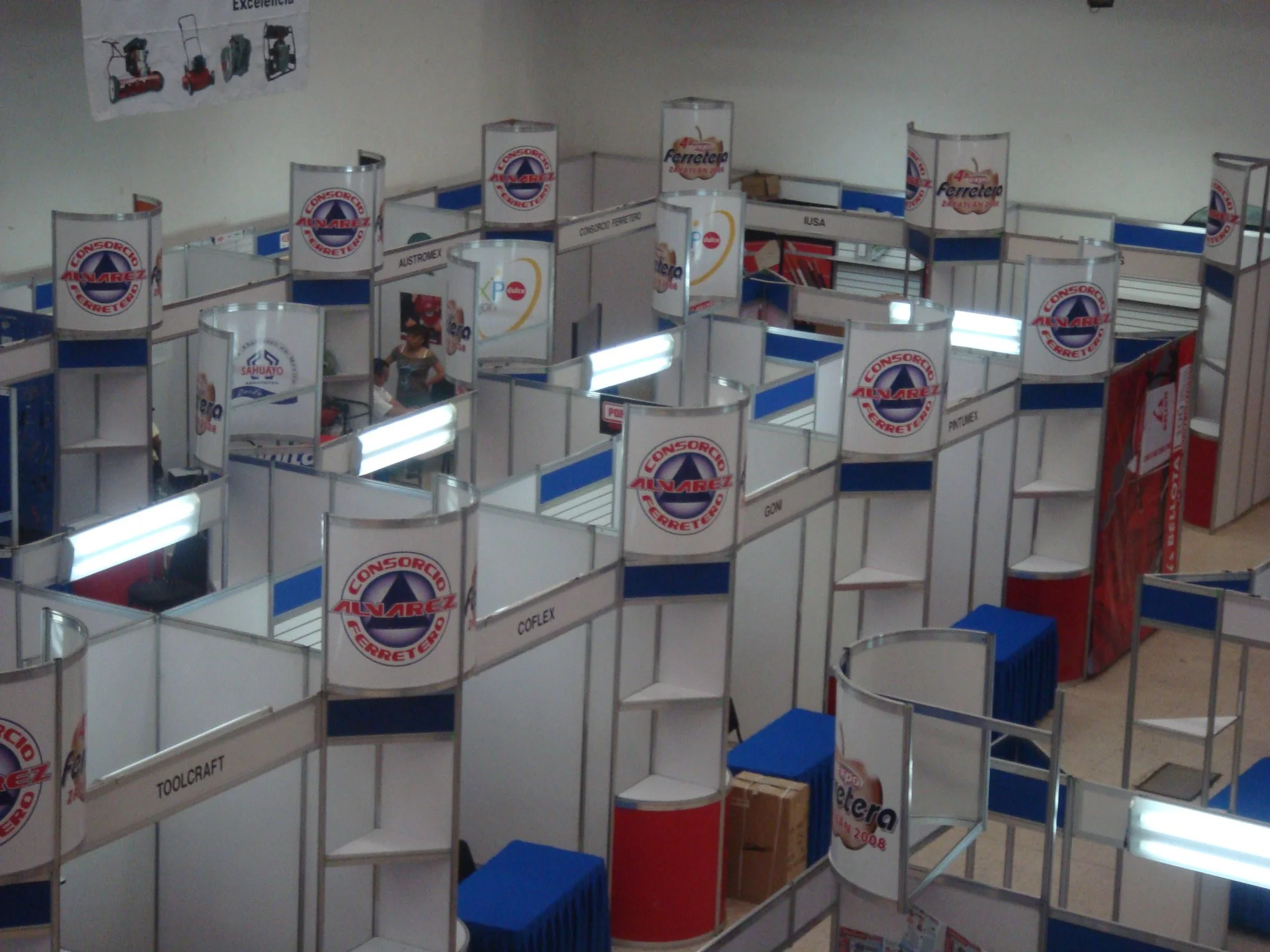 Exposición con puestos de diferentes empresas, algunos con logos y nombres como 'Consorcio Alvarez', 'Toolcraft', y 'Ferretería'.