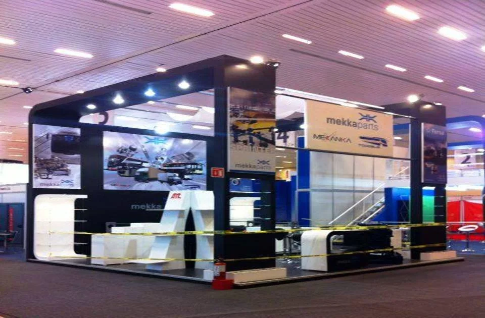 Stand de exhibición de piezas de automóviles en un aeropuerto o centro comercial, delimitado con cinta amarilla y señales de 'mekkaparts'.