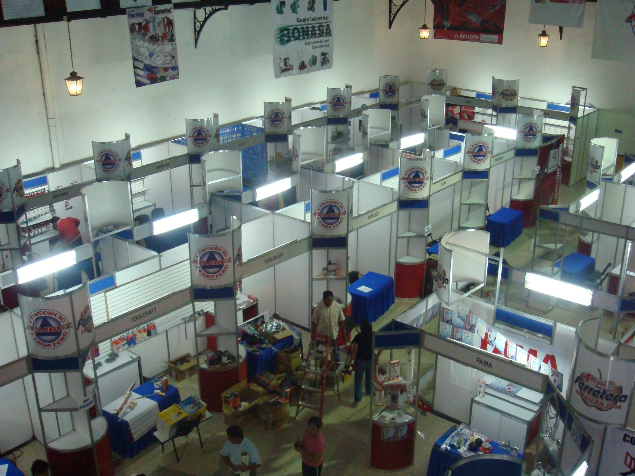 Vista aérea de una feria o expo con varias stands y empleados armando los puestos, algunos visitantes en el área.