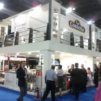 Imagen de un stand en una feria o exposición, con varias personas interactuando y un cartel que dice 'Costeña' en la parte superior.