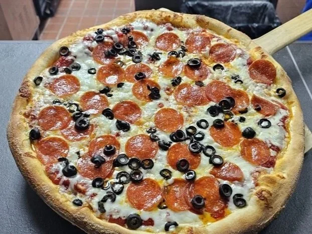A large pepperoni and black olive pizza on a pizza peel.