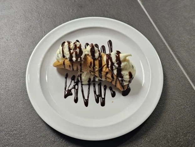 Banana split with vanilla ice cream, chocolate syrup, and banana on a white plate