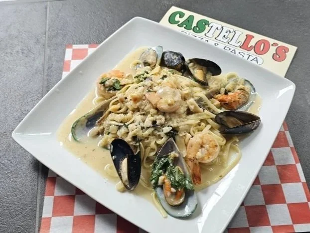Plate of seafood pasta with shrimp, mussels, and fettuccine, served on a white square plate with a restaurant card in the background.
