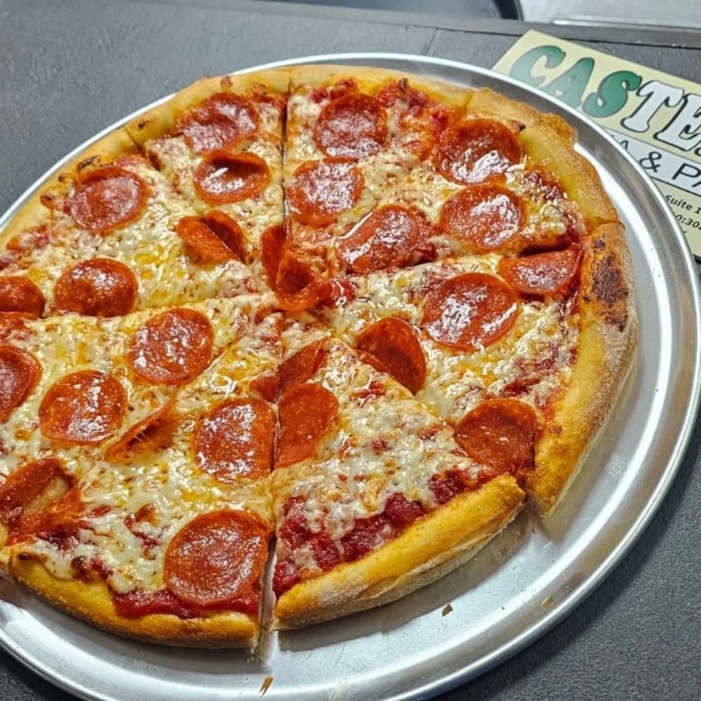 A pepperoni pizza on a metal tray with a few slices missing, on a dark table.