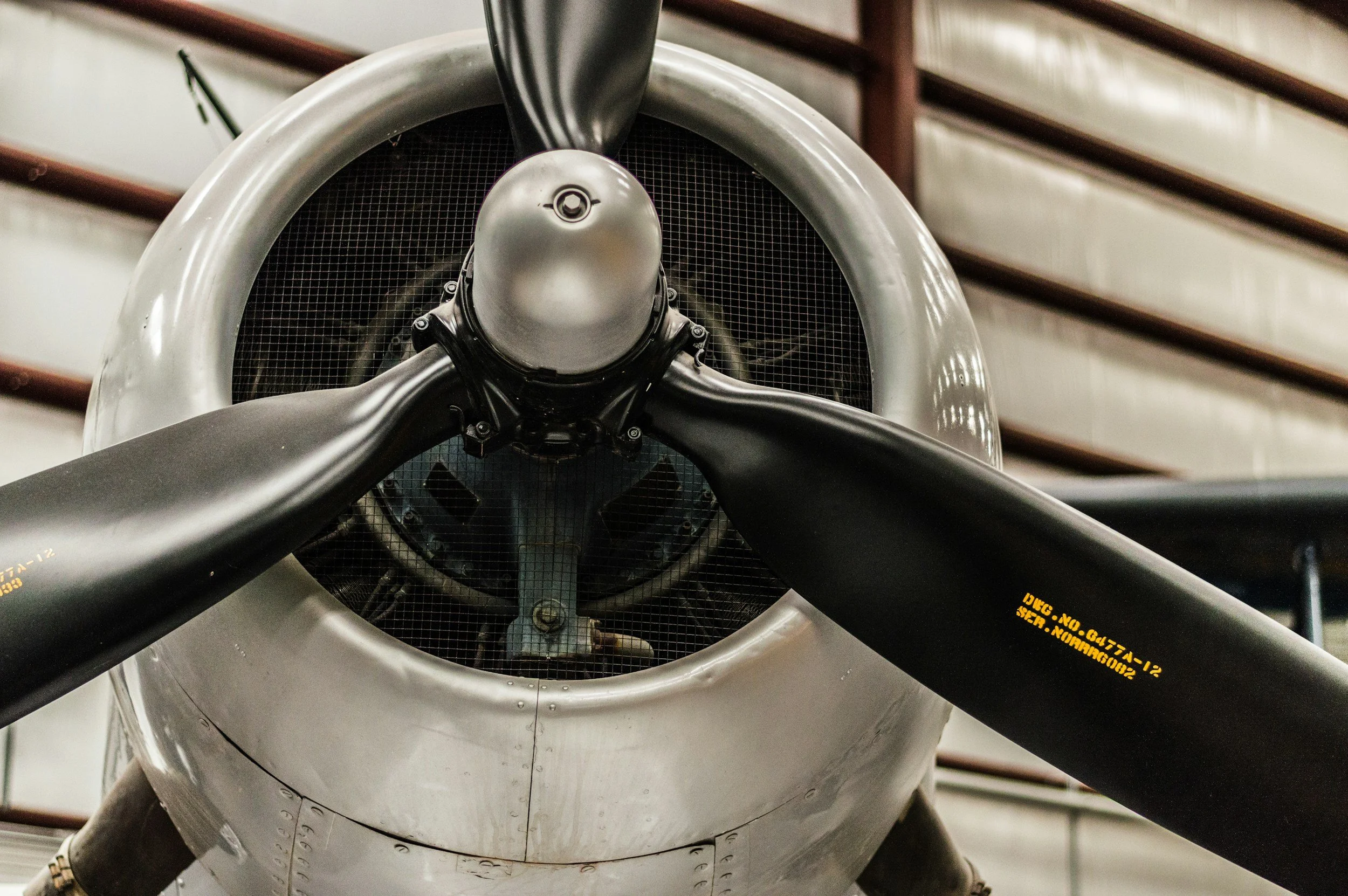 Close-up view of the front of a vintage airplane showing its propeller, engine cowling, and propeller hub inside an aircraft hangar.