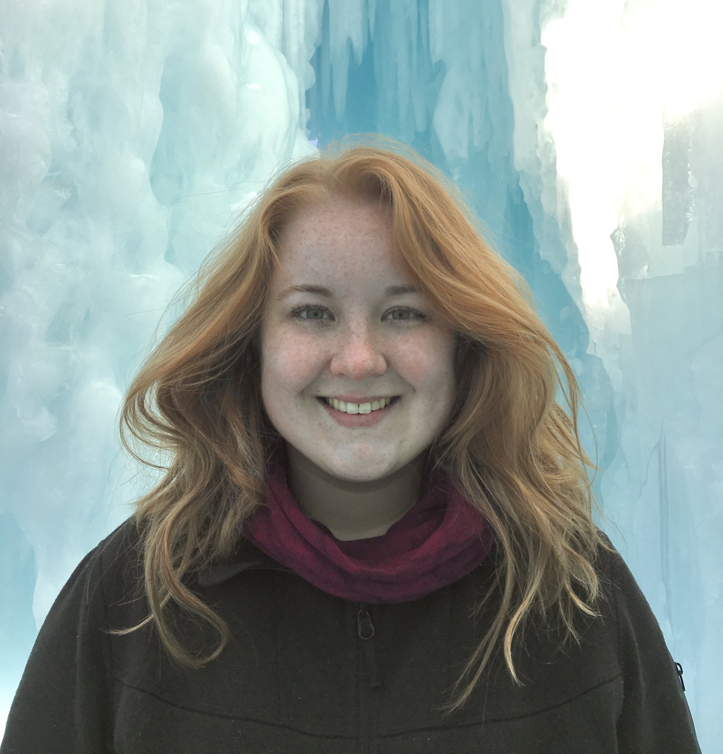 Young woman with red hair smiling in front of blue ice formations
