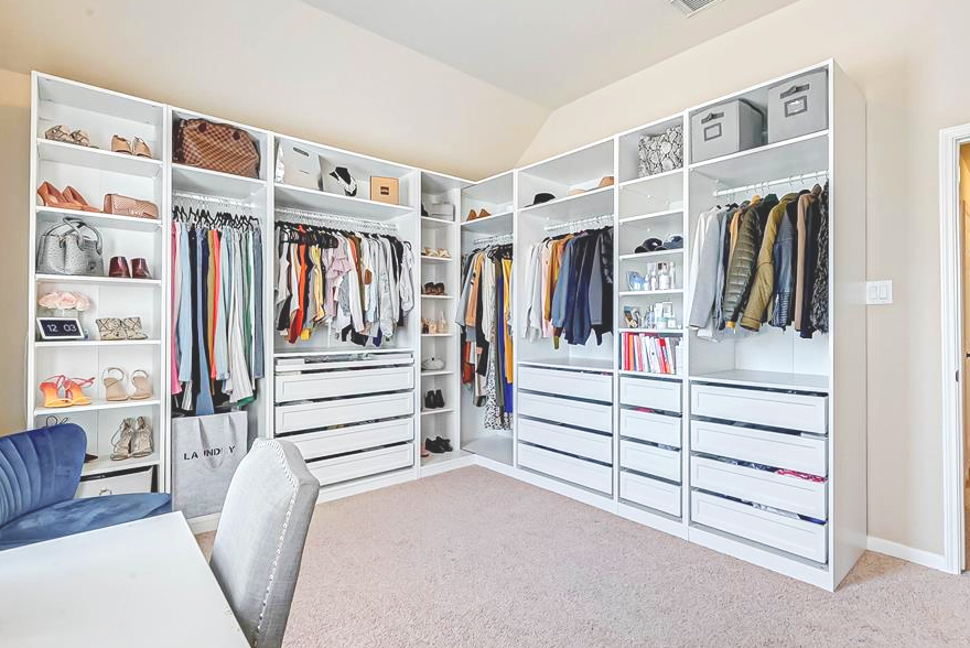 A walk-in closet with built-in white shelves and drawers, displaying shoes, handbags, clothing, books, and storage boxes.