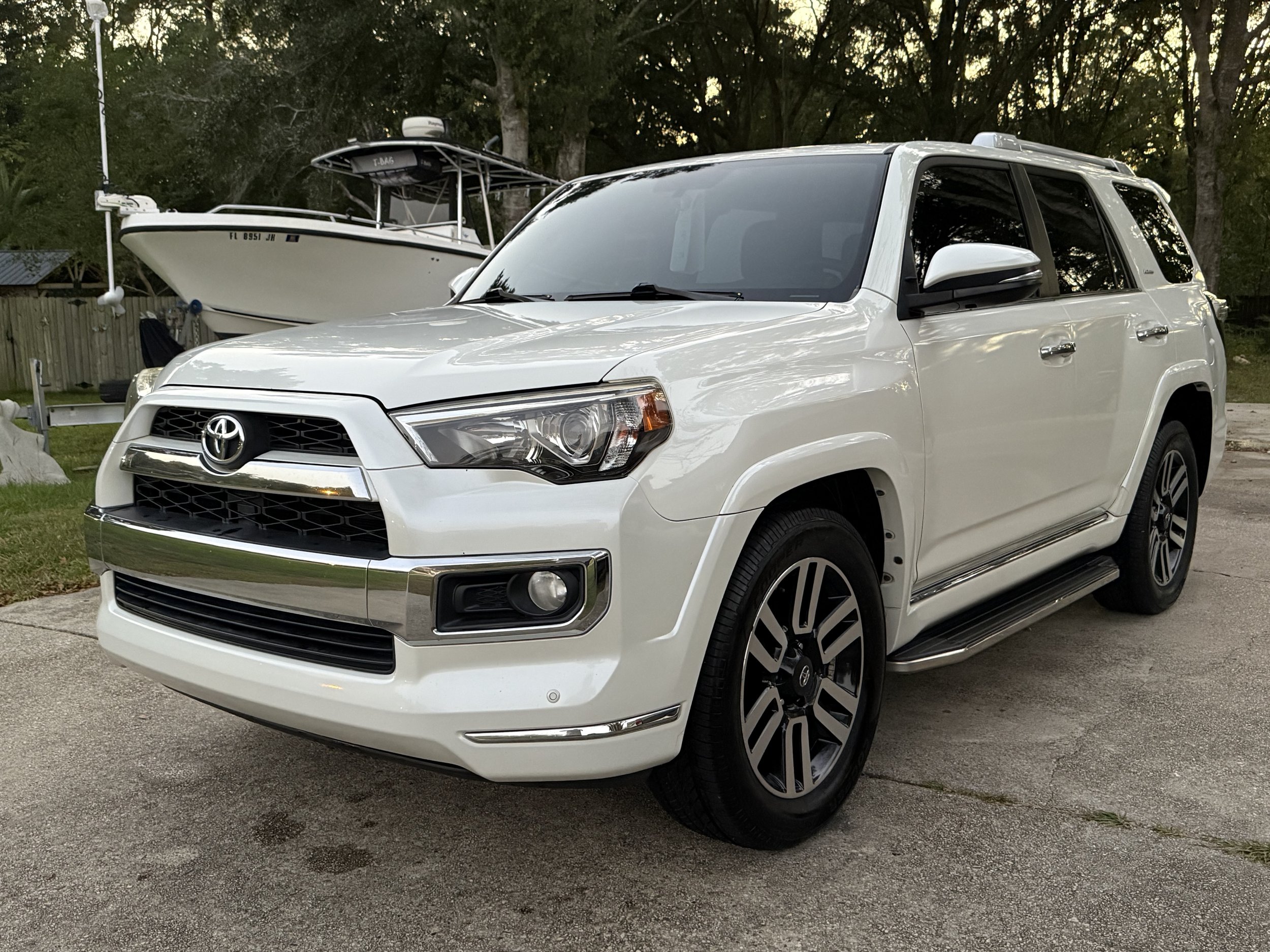 White Toyota SUV parked on a driveway with a boat in the background and trees around.