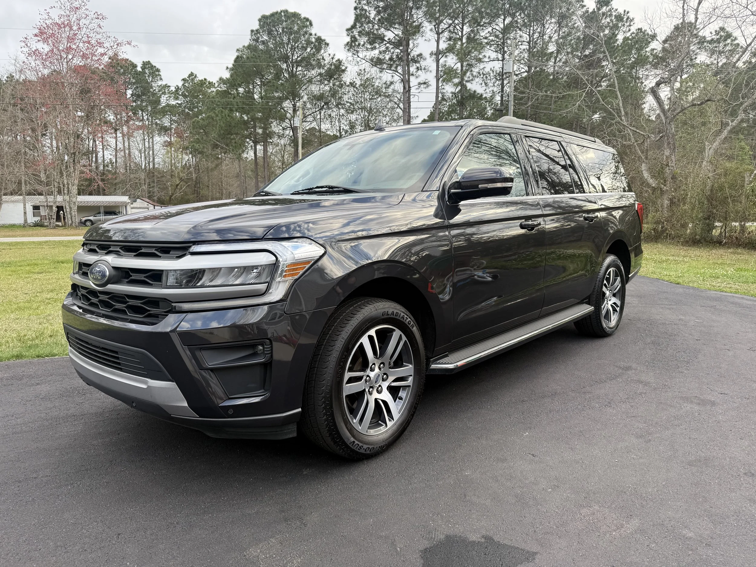 A black Ford SUV parked on a paved driveway with a grassy yard and trees in the background.