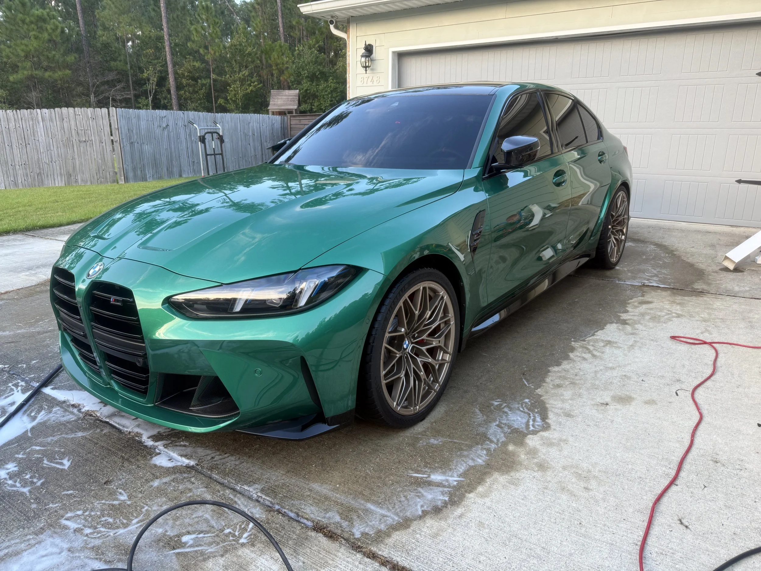 A green sports car parked outside a house being washed, with soap suds on the ground and a red hose nearby.