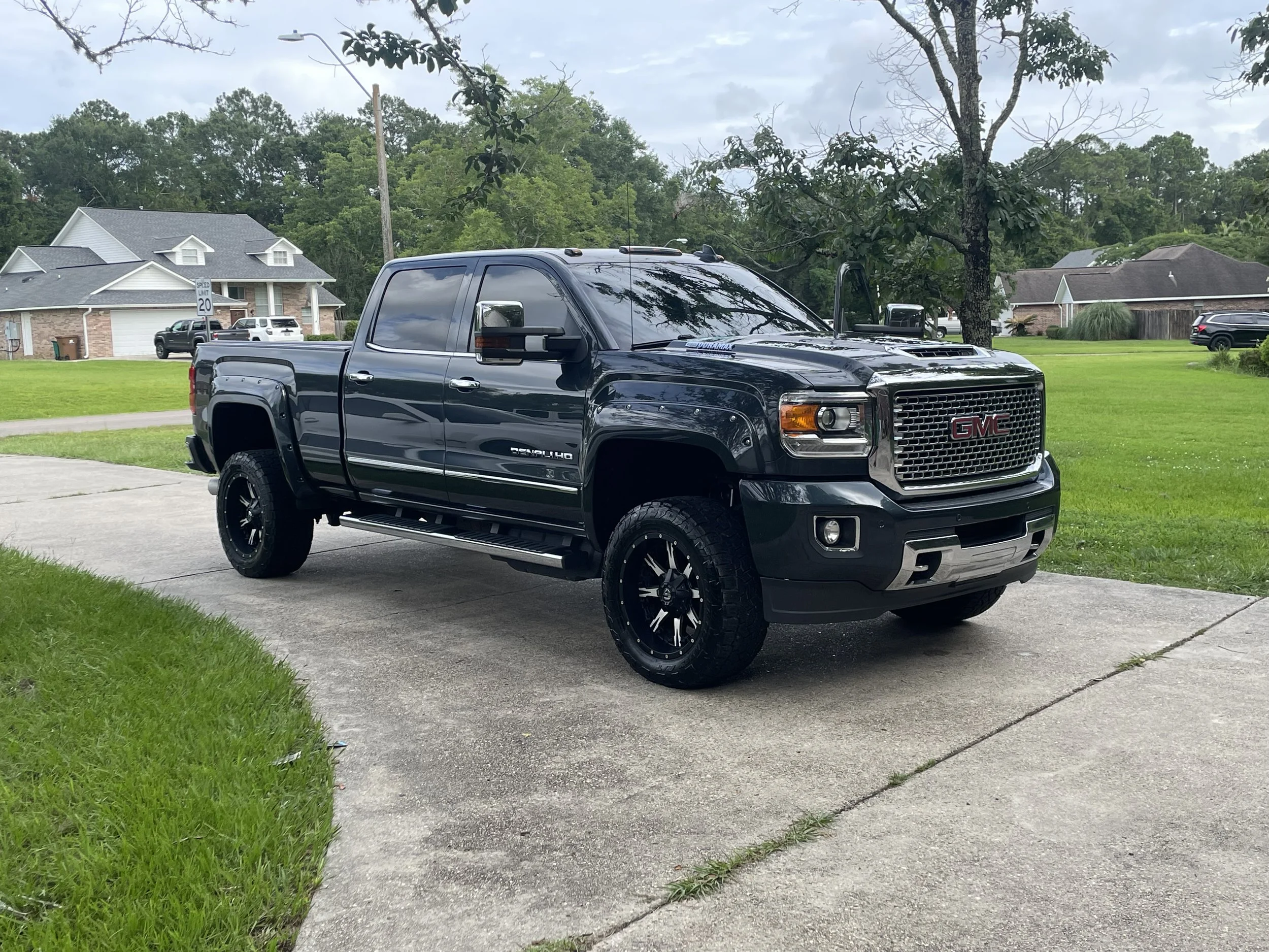 A black GMC Denali truck parked on a residential driveway with houses and green lawns in the background.