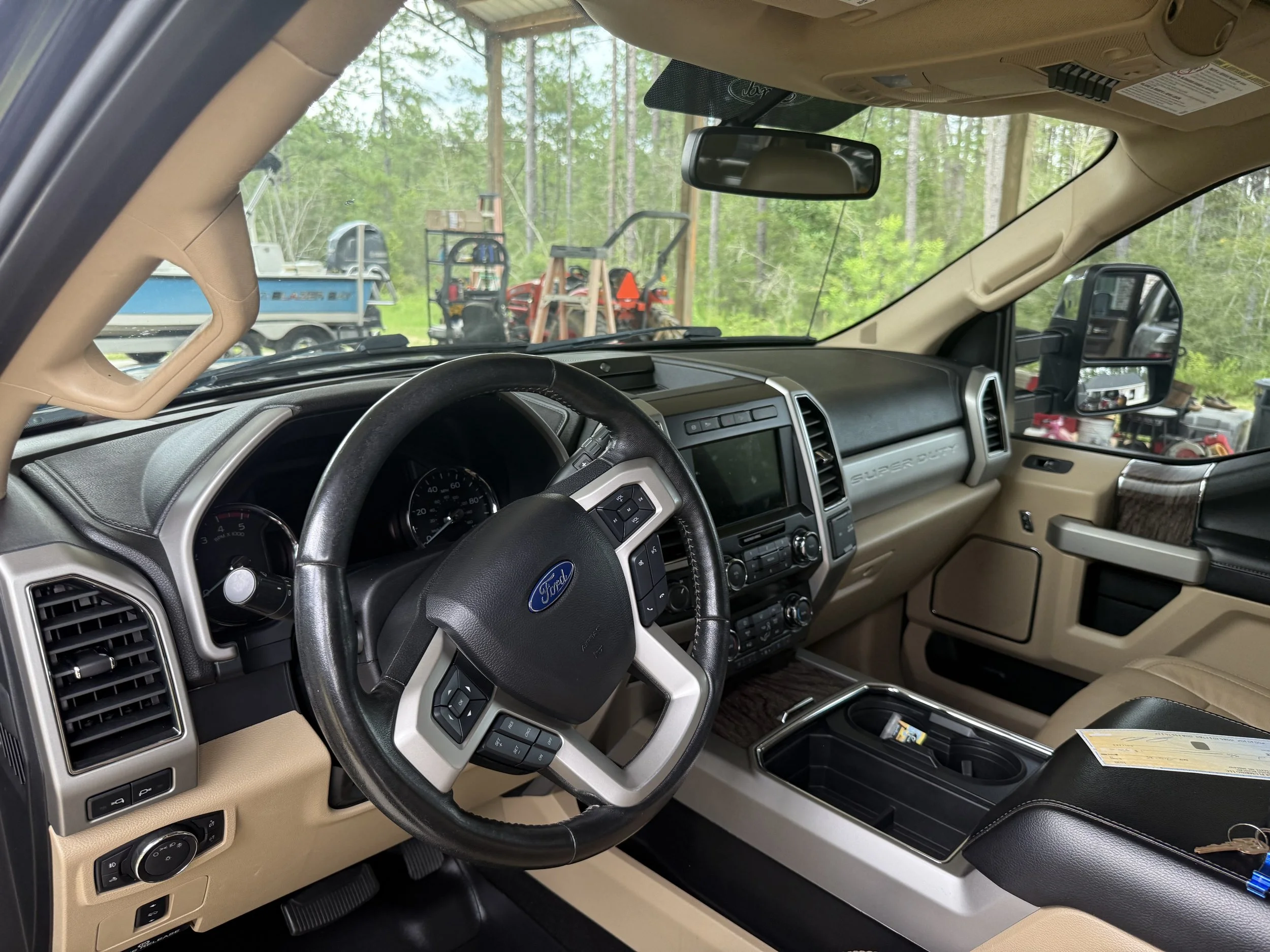 Interior of a Ford vehicle, showing black steering wheel, dashboard, gear shift, and beige seats with wood accents.