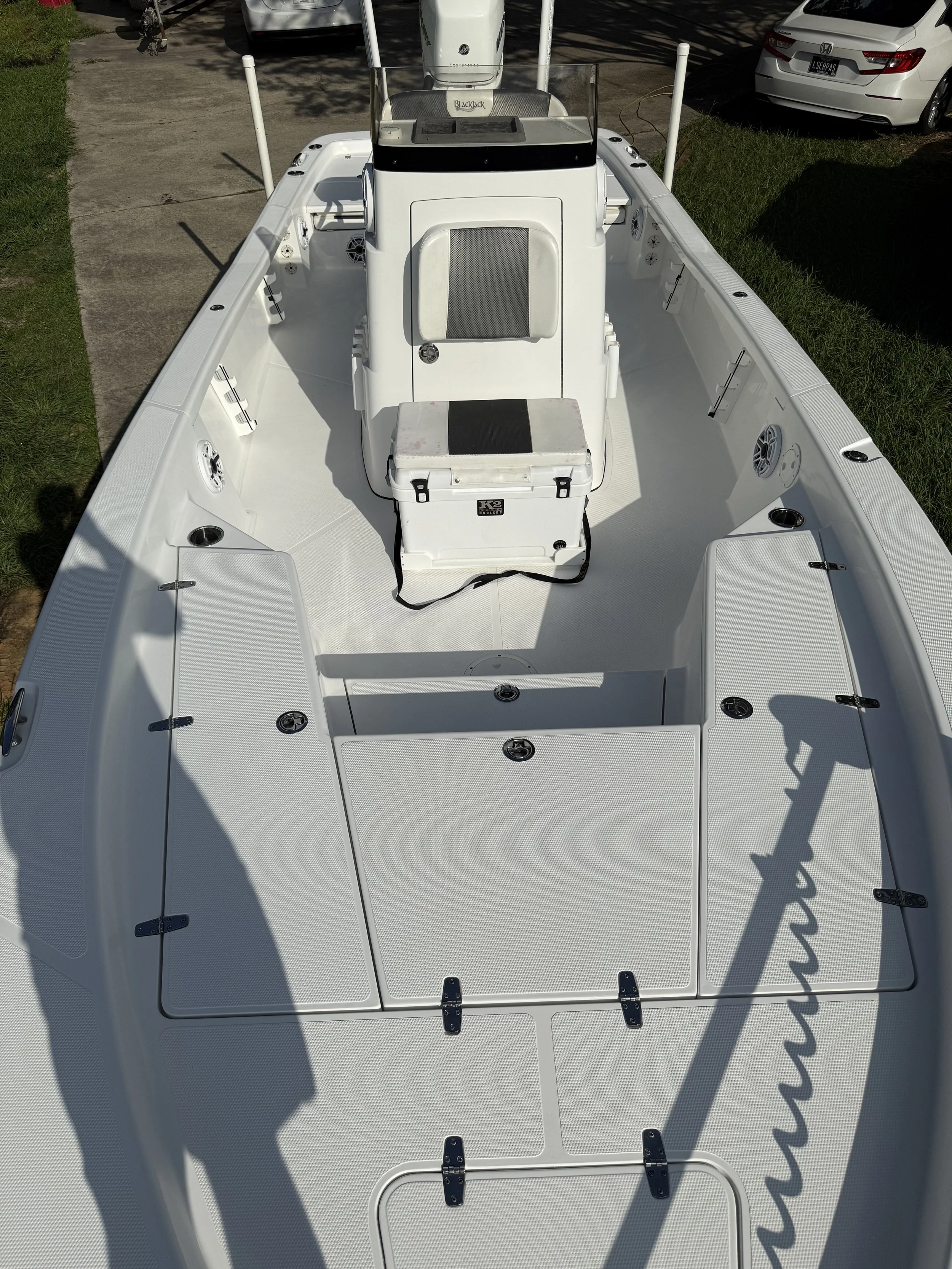 Top view of a white fishing boat on land, showing deck compartments, a steering console, and an outboard motor.