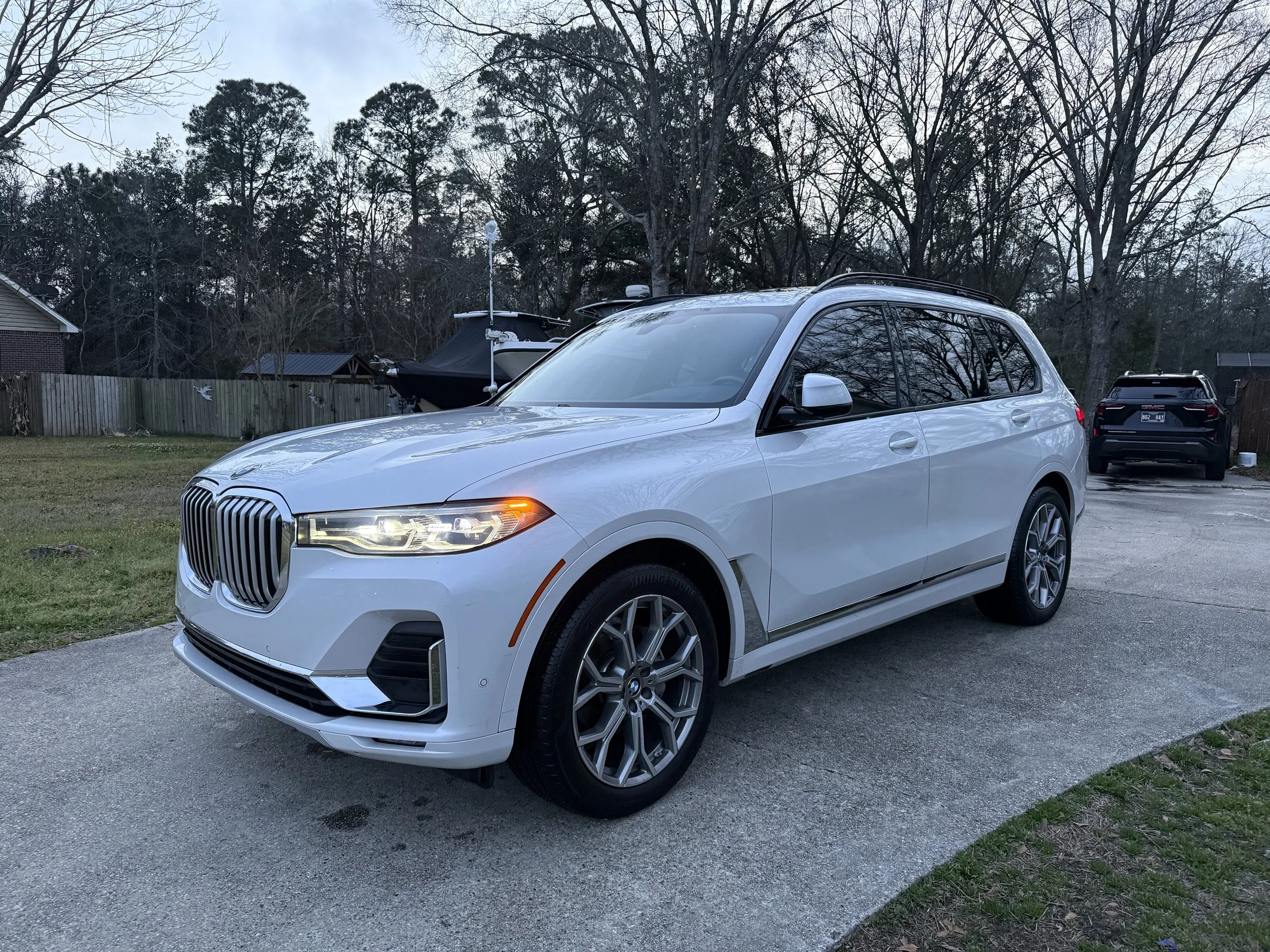 Silver BMW SUV parked on a driveway with trees and houses in the background.