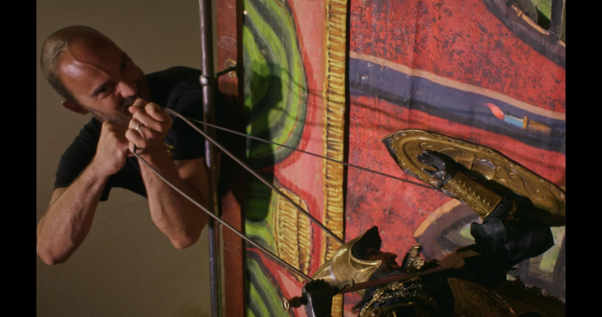 A puppeteer wearing black shirt and glasses animating a pupo with a snake and a colorful, patterned fabric backdrop.