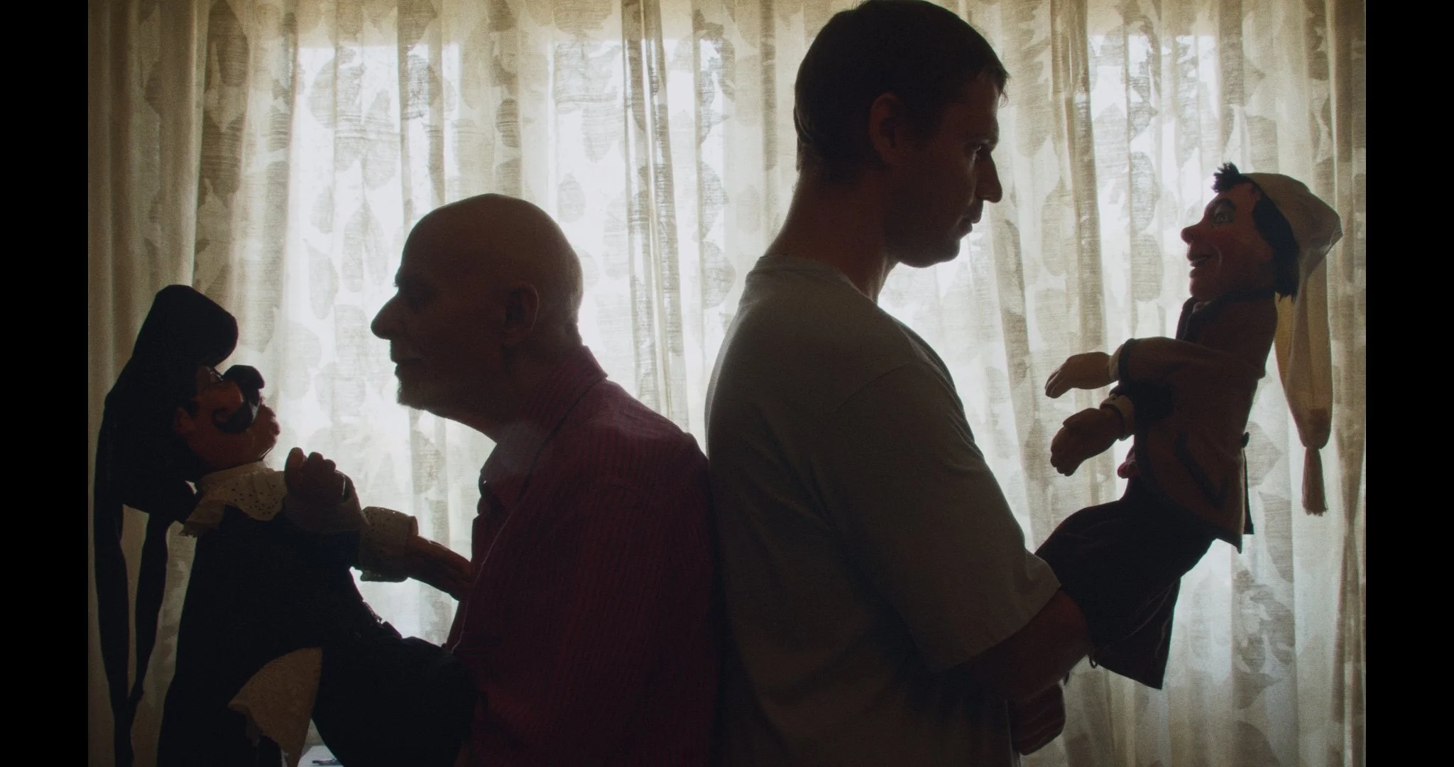 Silhouettes of two puppeteers holding puppets against a window with curtains.