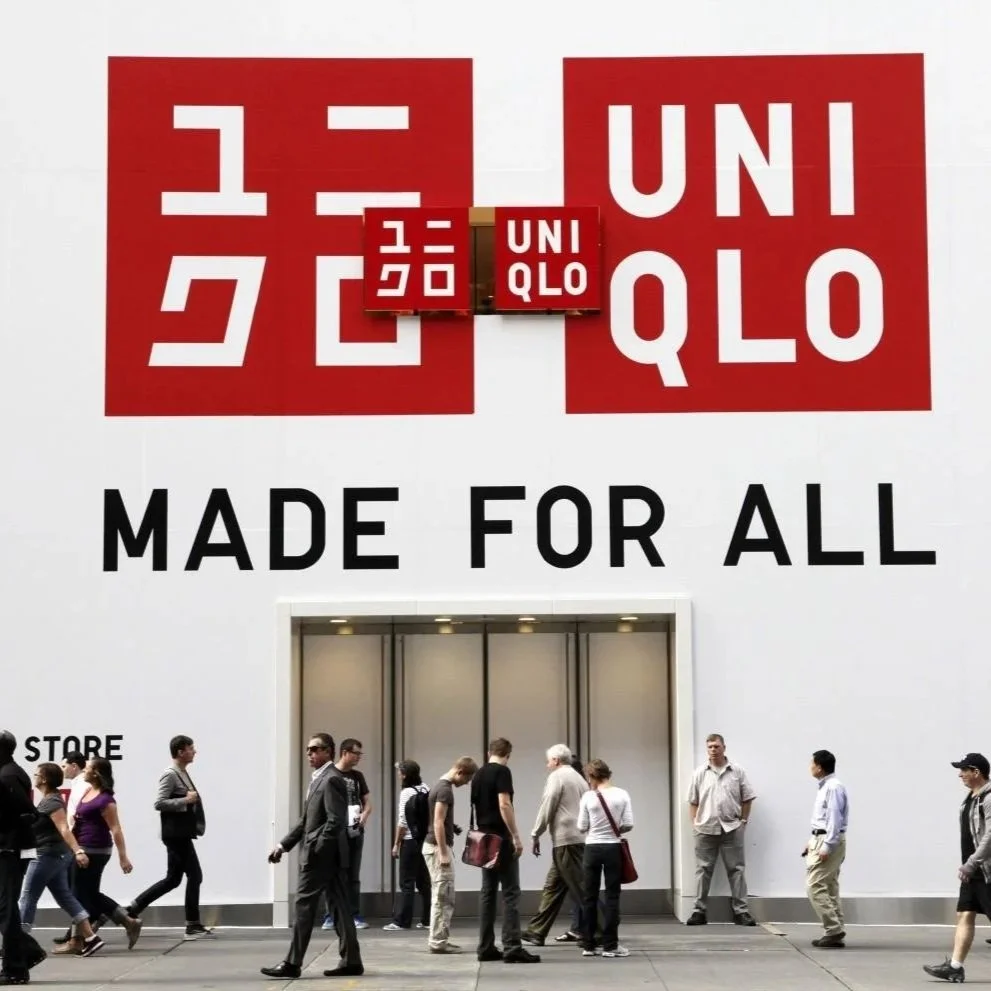 People walking past a large retail store with a graphic sign promoting the brand UNIQLO and the slogan "Made for All" on the exterior wall.