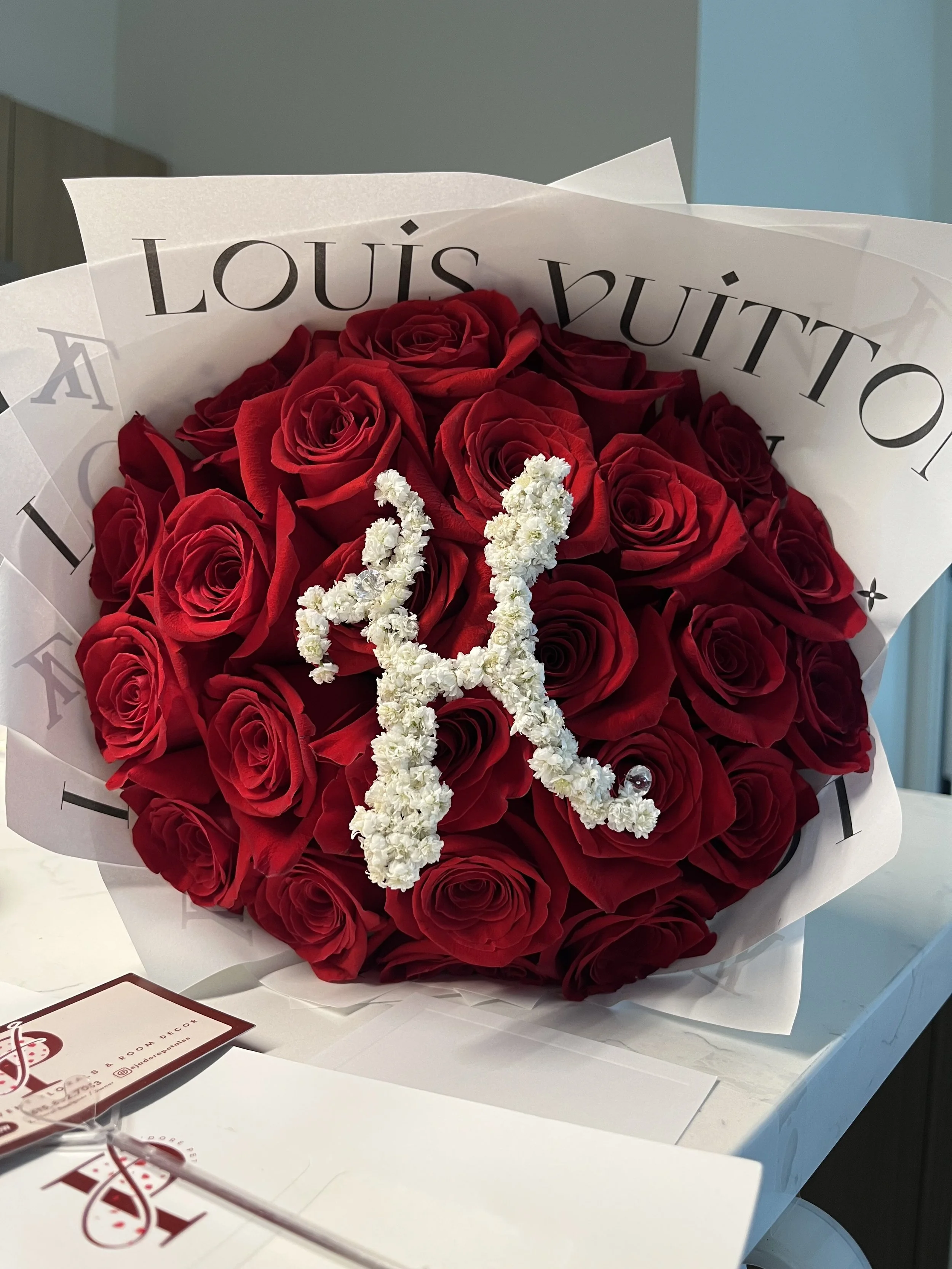 Bouquet of red roses wrapped in white paper with a white flower garland shaped like a star on top.