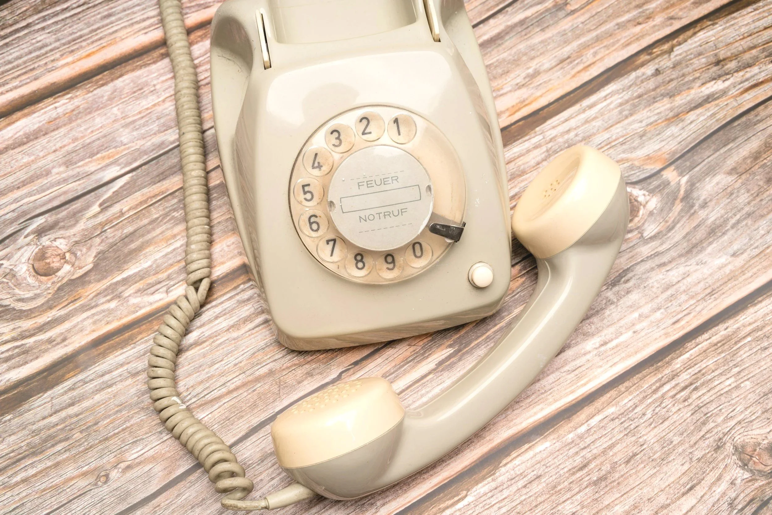 An old-fashioned rotary dial telephone lying on a wooden surface.