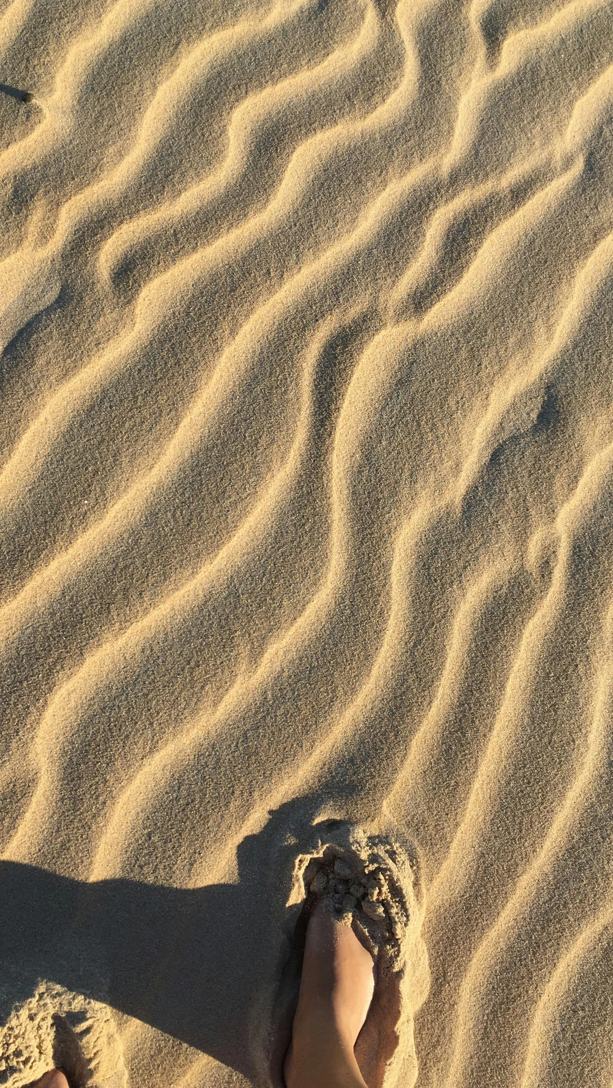 Footprints in the sand on a beach or desert with rippled sand patterns.