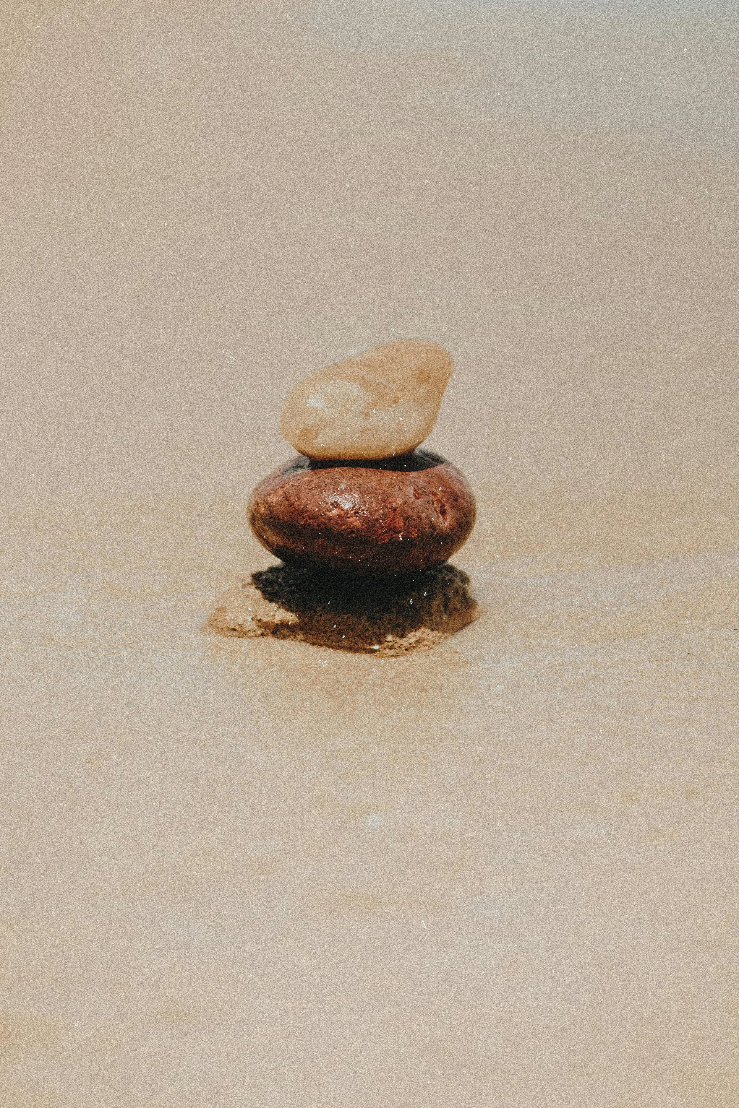 Three stacked stones on sand with a neutral background.